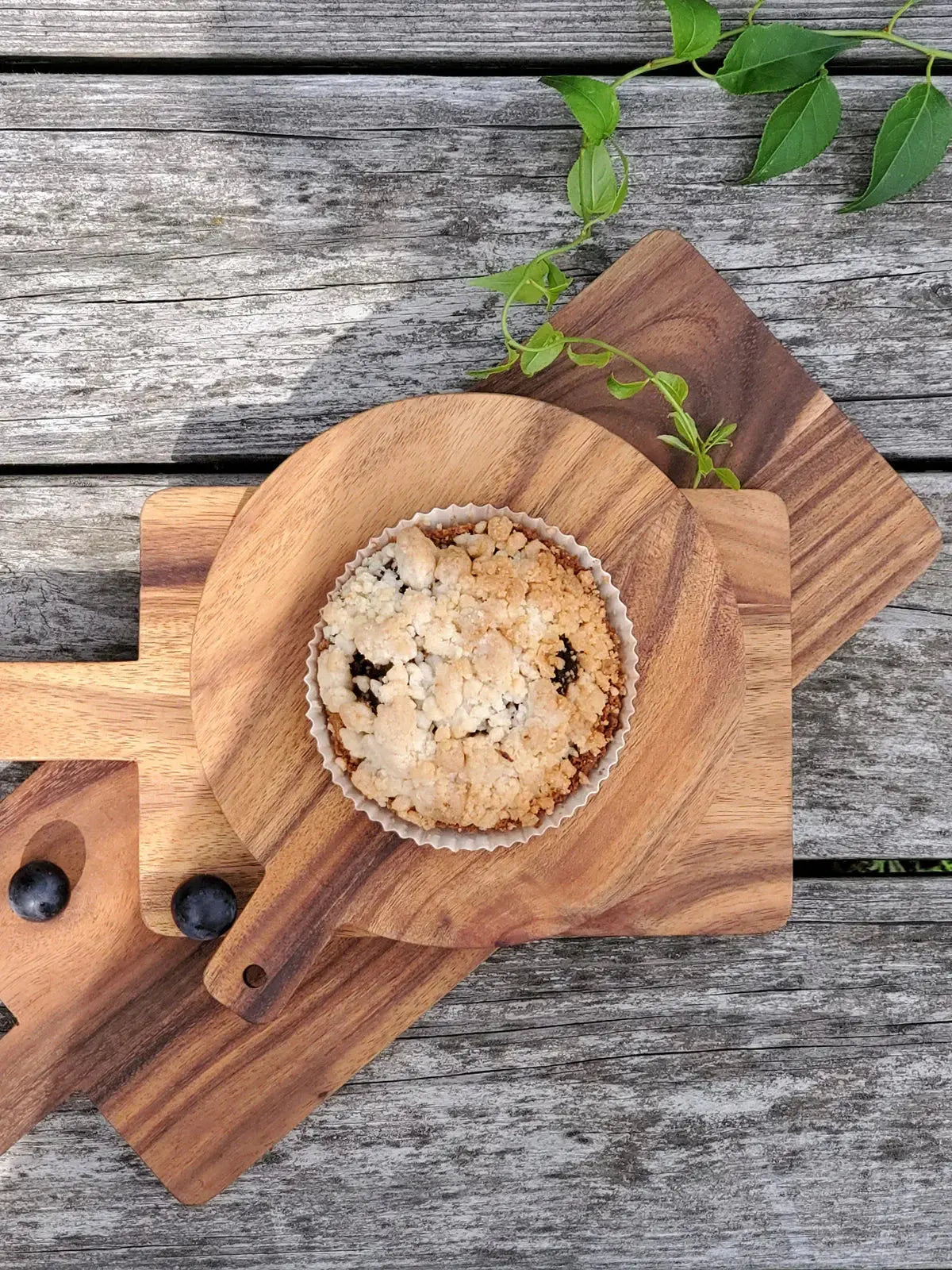 Blueberry crumble tart on rustic wood cutting boards with fresh green leaves, cozy farmhouse decor