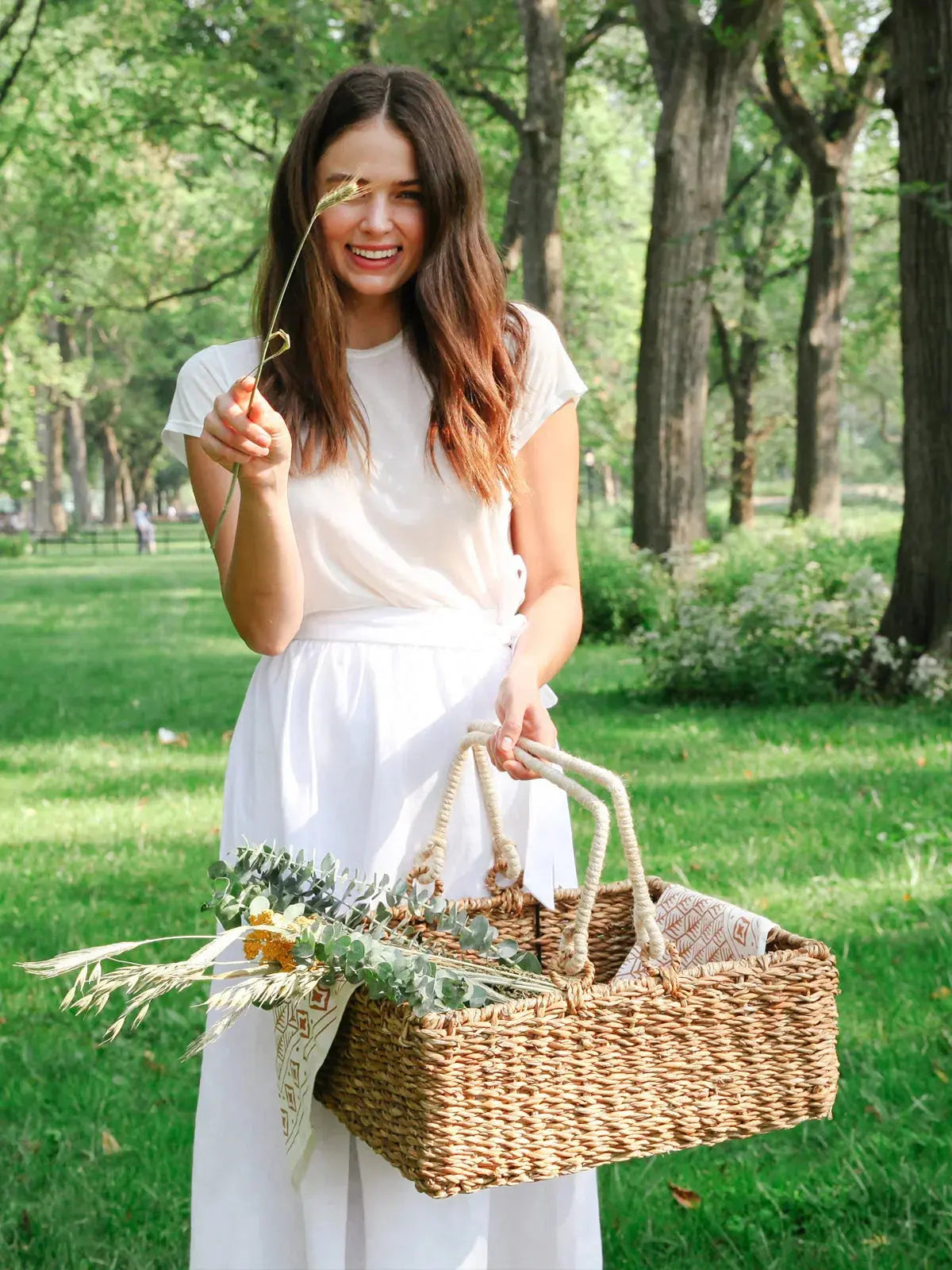 Woman holding woven basket with dried flowers in park, farmhouse style decor