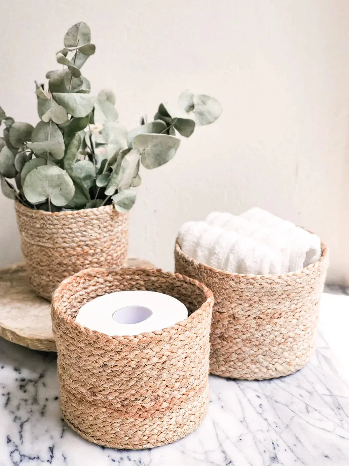 Woven seagrass baskets holding eucalyptus, towels, and toilet paper for cozy farmhouse bathroom decor