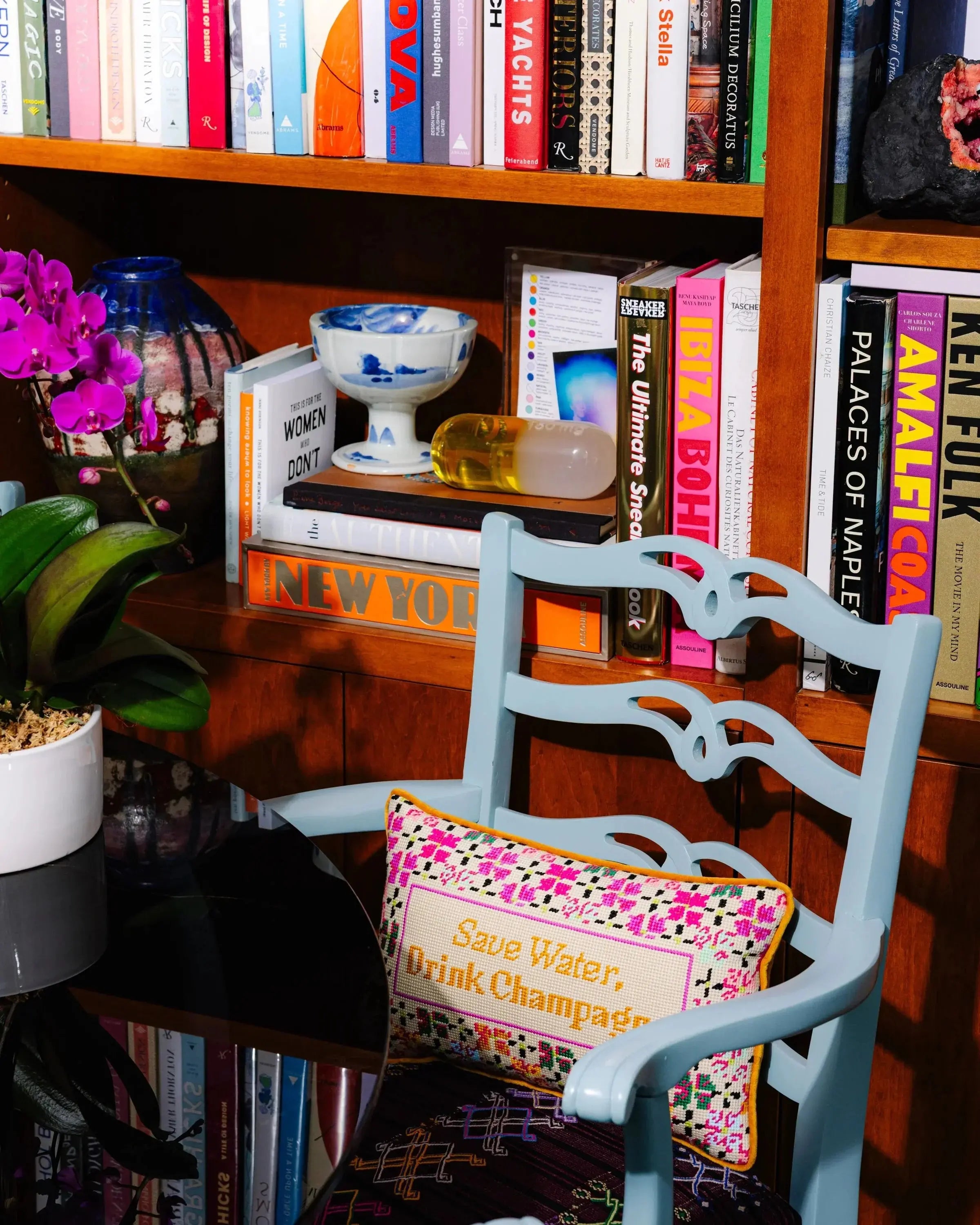 Chair with a colorful cushion in front of a bookshelf filled with books and decorative items.