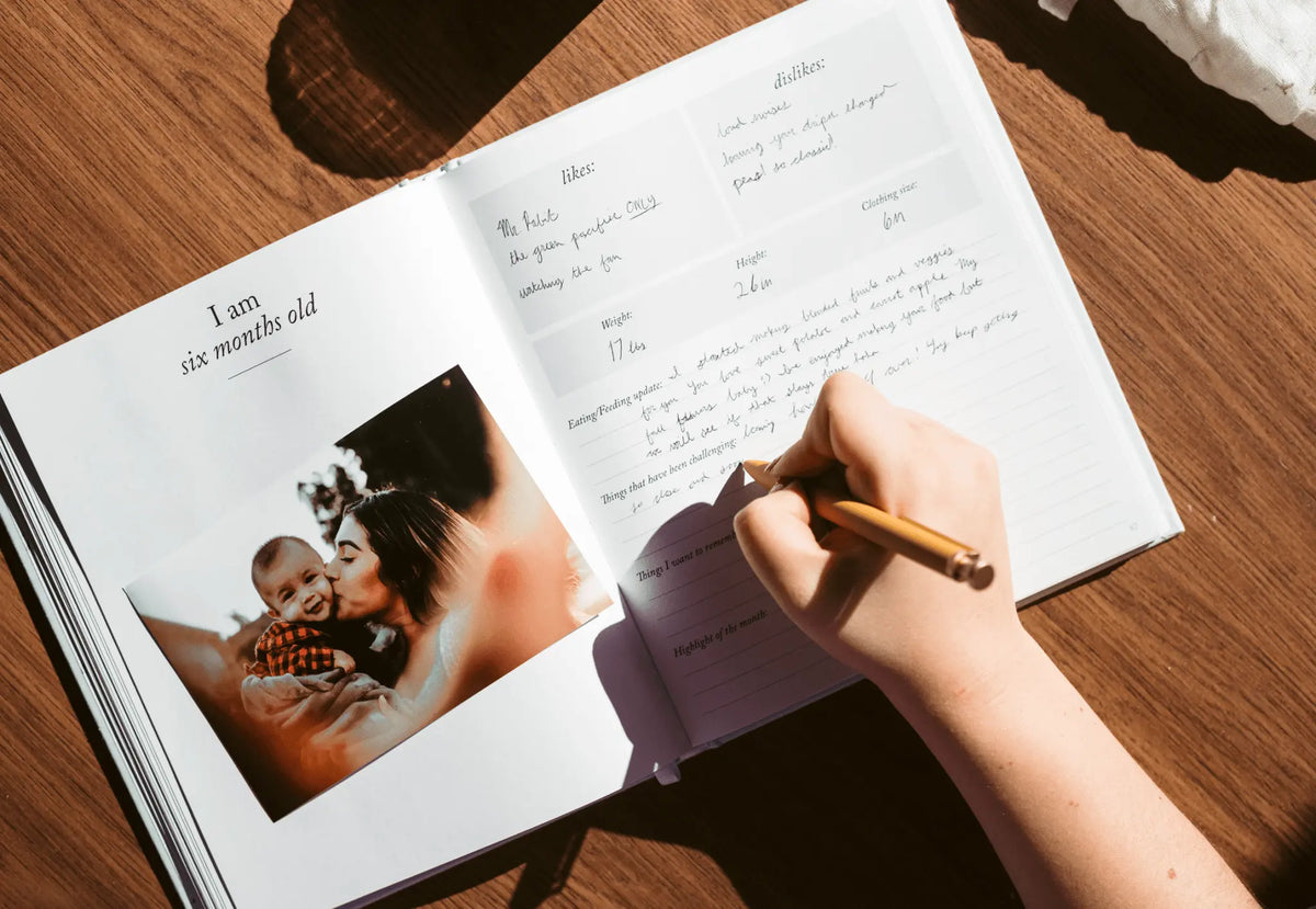Open book with a photo of a baby and text, being written on with a pen.
