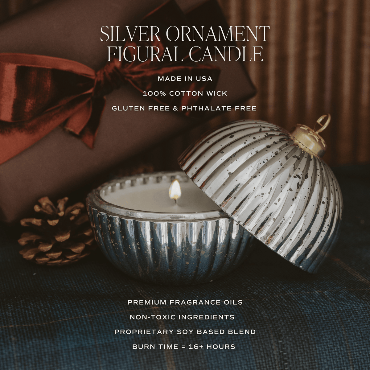 Silver ornament-shaped candle with its ribbed dome lid propped open beside the lit candle vessel, shown in a styled holiday setting with a brown gift box, ribbon, pinecone, and dark fabric background. Text on the image reads 'Silver Ornament Figural Candle' with additional product claims.