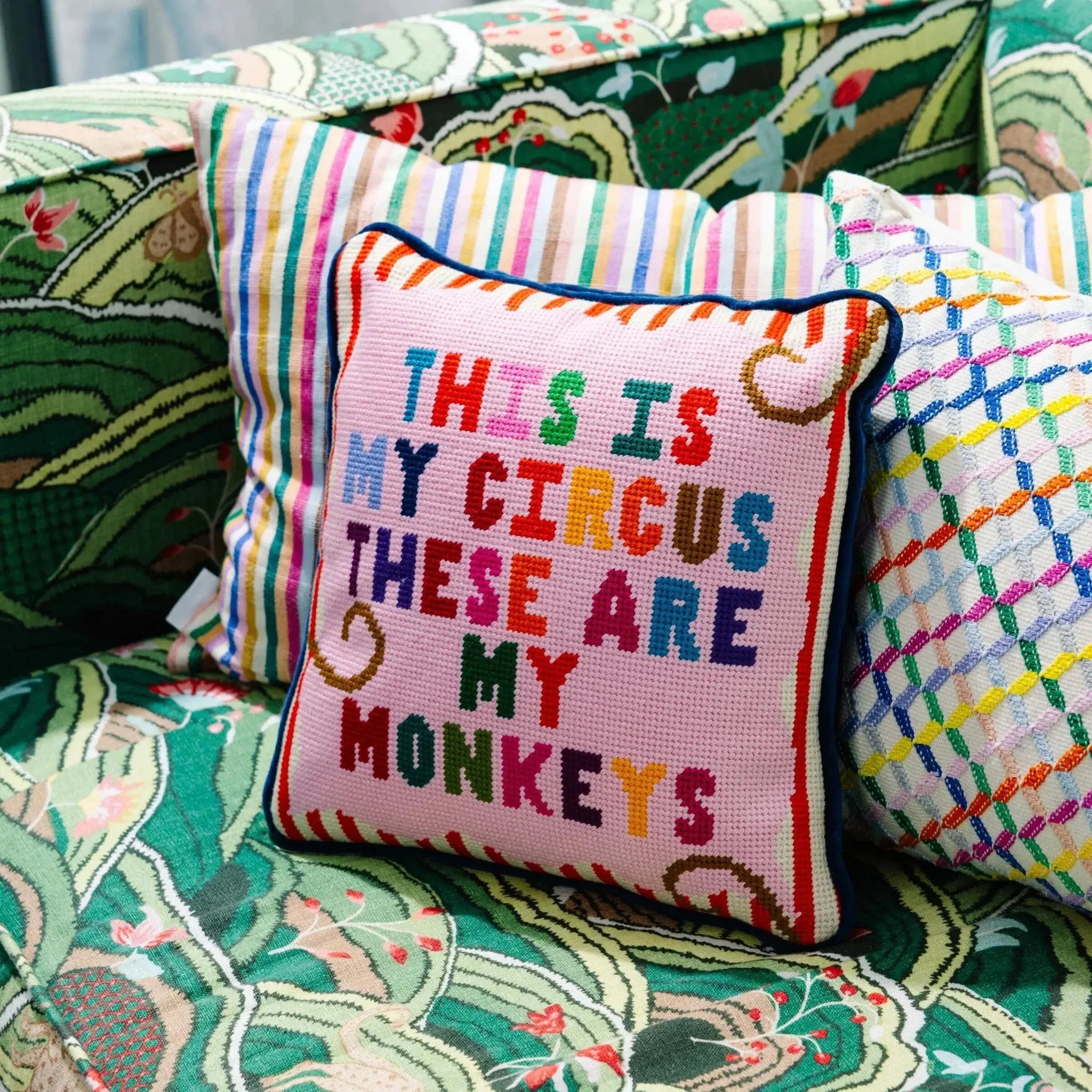 Colorful needlepoint pillow with 'This is my circus, these are my monkeys' quote on cozy patterned sofa