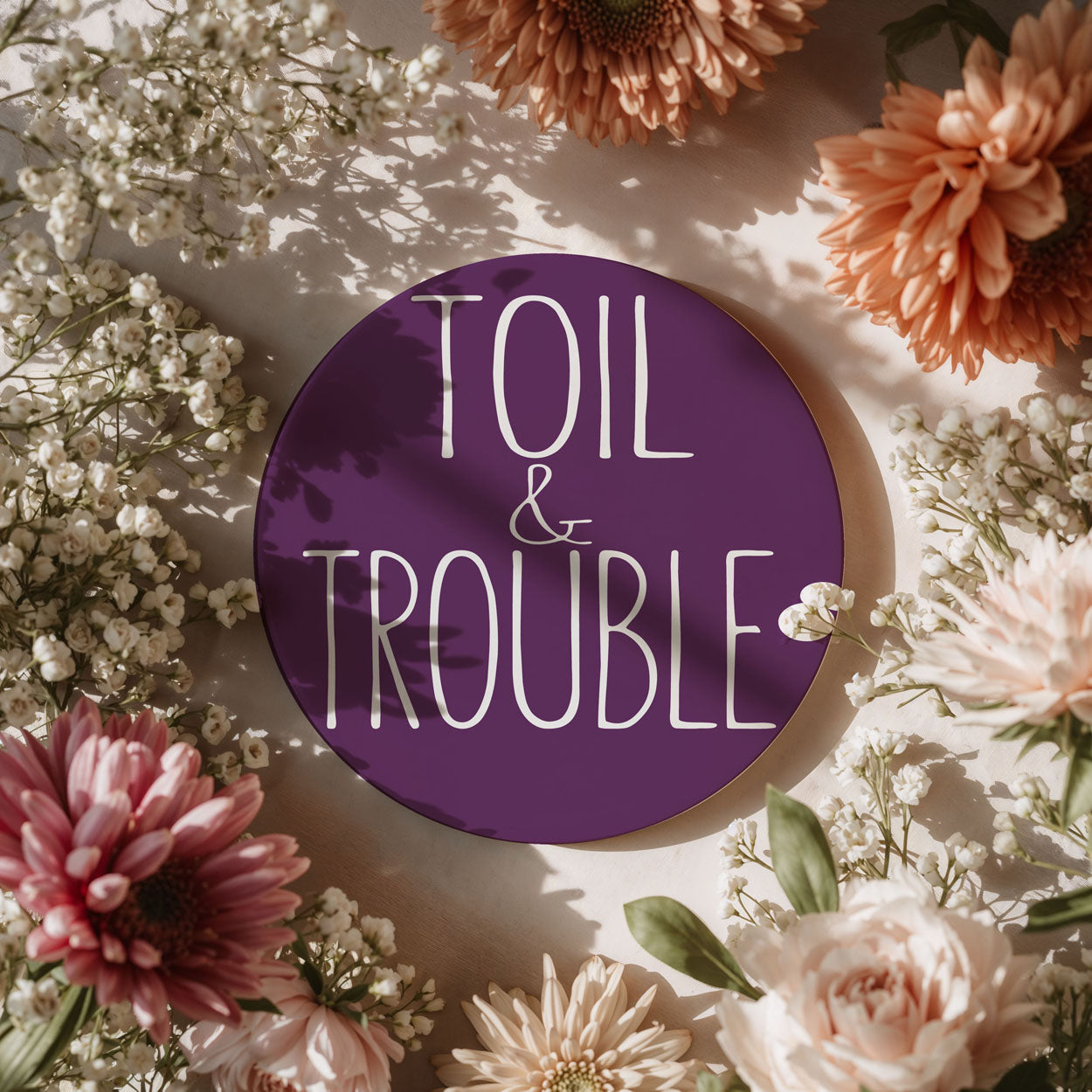 Purple round sign with 'TOIL & TROUBLE' text surrounded by flowers