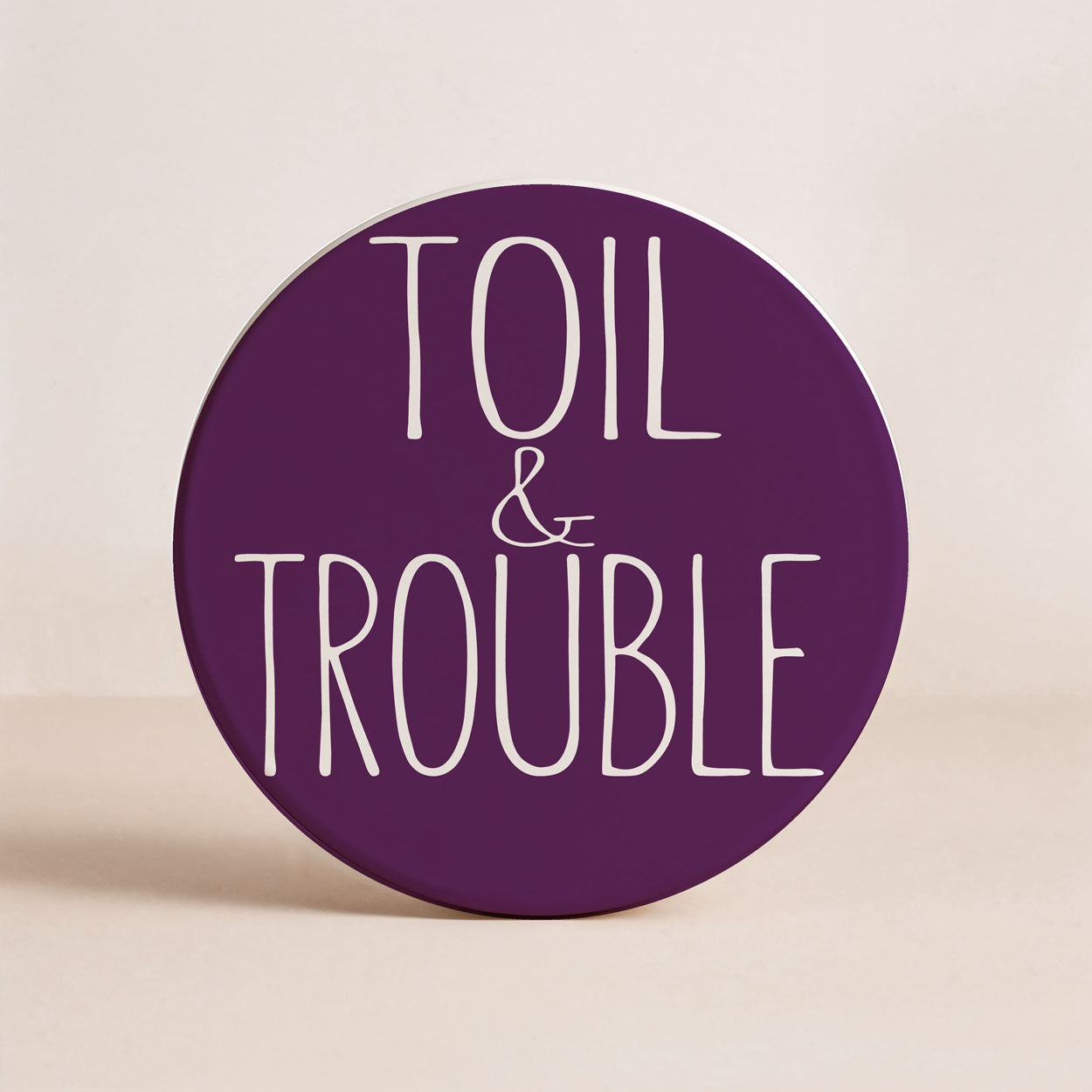 Round purple sign with 'TOIL & TROUBLE' text on a beige background