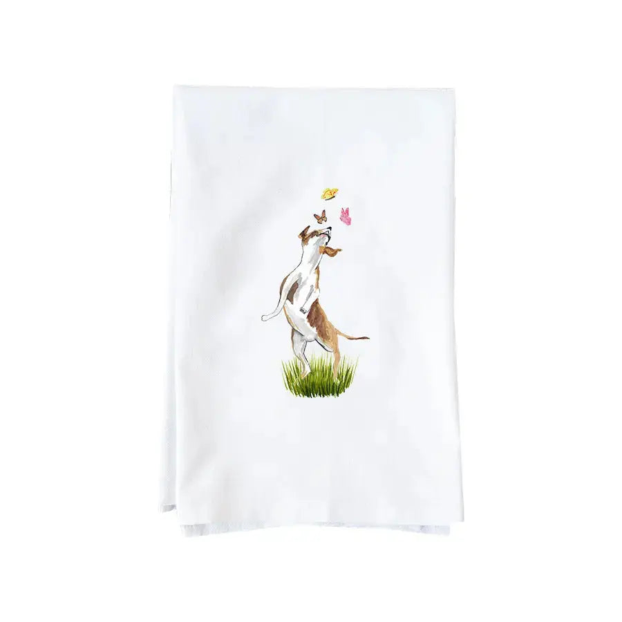 A white kitchen tea towel featuring a watercolor illustration of a white and brown dog standing on its hind legs to catch a butterfly above green grass.