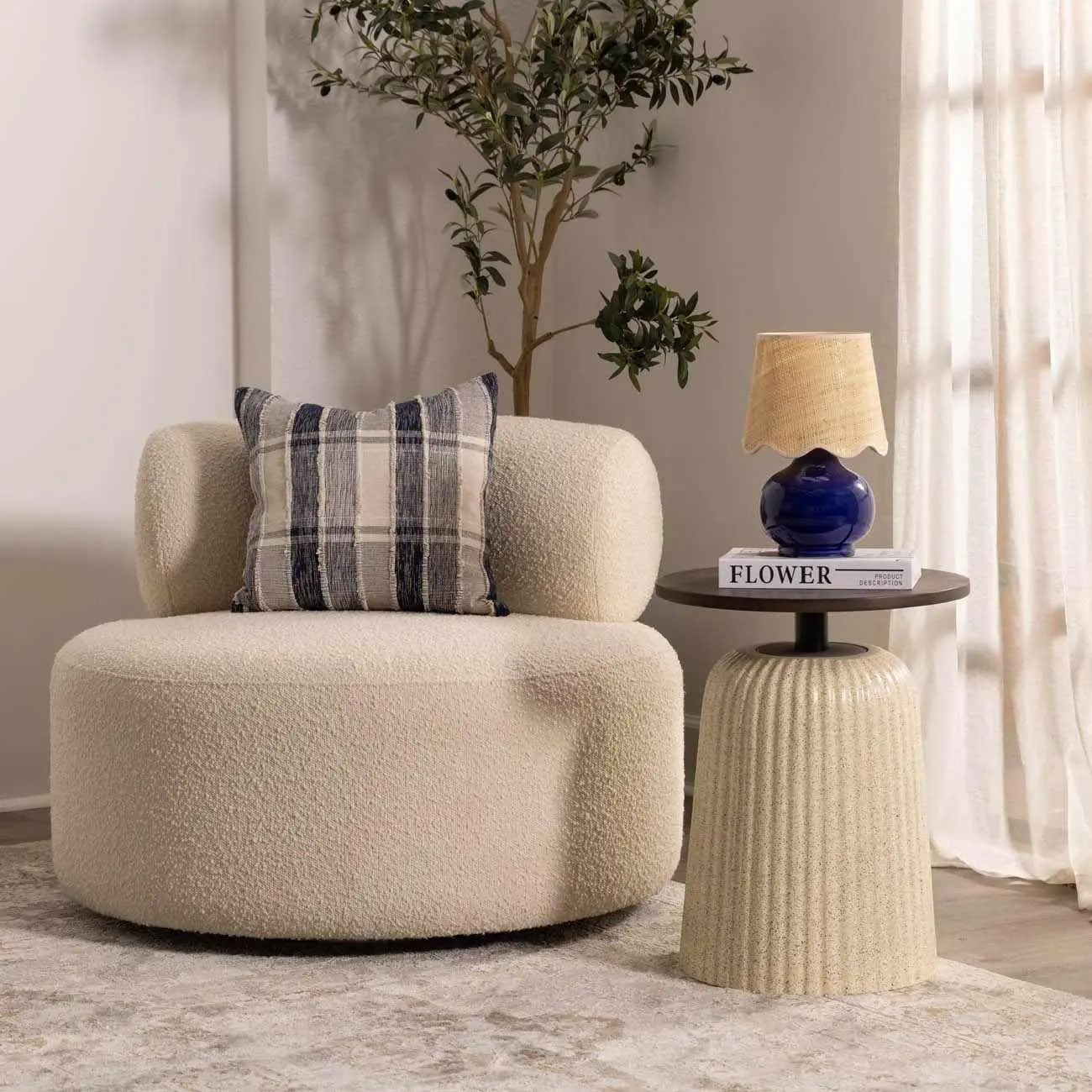 Cozy beige bouclé armchair with plaid pillow, beside side table with blue lamp and plant, farmhouse living room decor