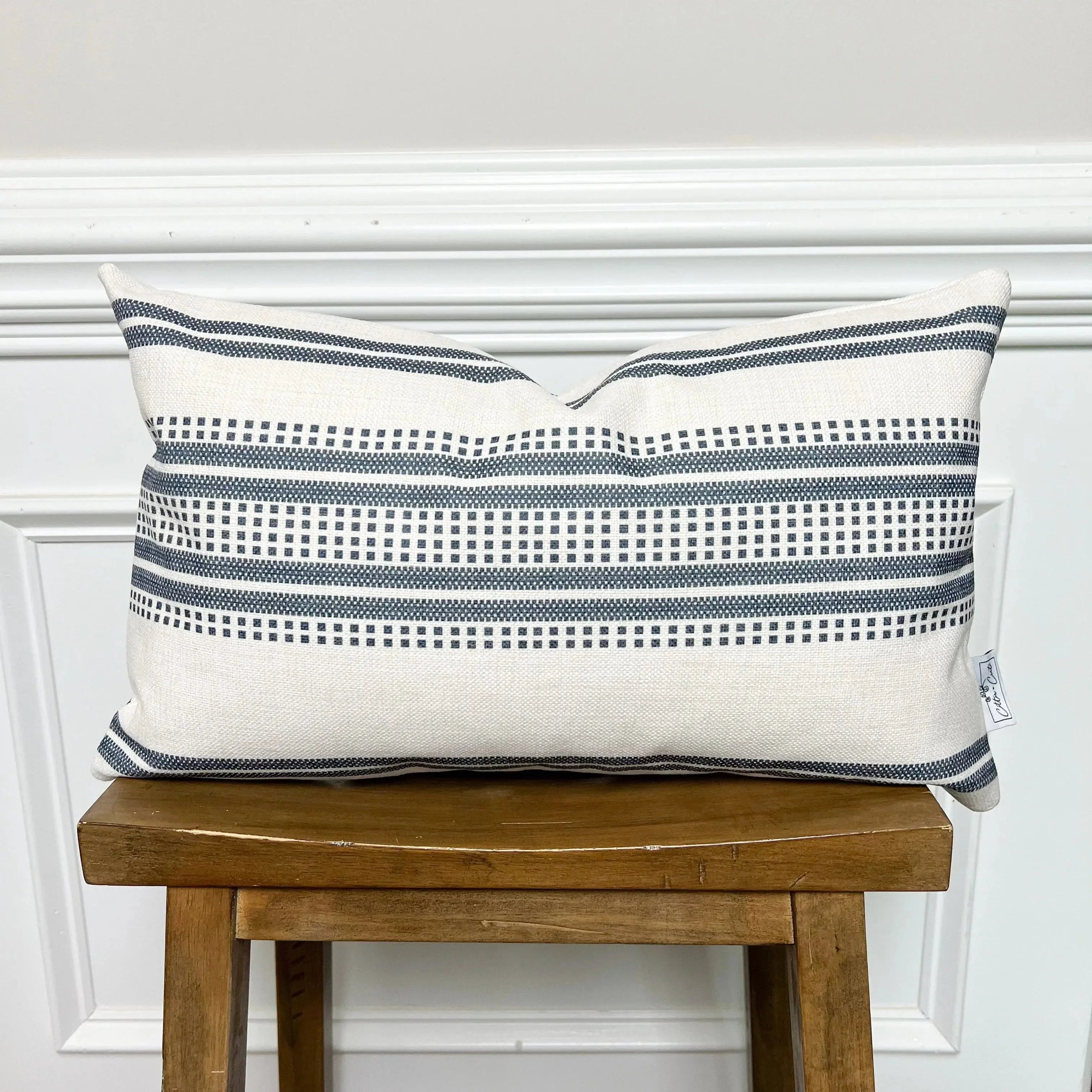 Cream and navy blue striped farmhouse pillow with geometric pattern, styled on wooden stool for cozy cottage decor
