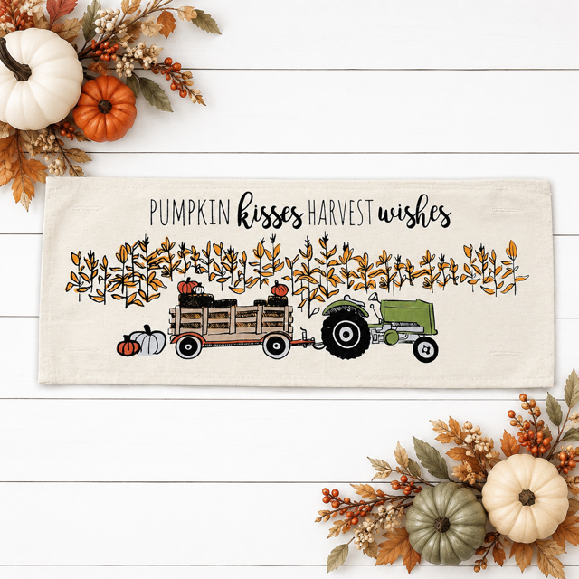 A rectangular cream-colored fabric sign or towel featuring a fall harvest illustration with the text 'PUMPKIN kisses HARVEST wishes.' The design shows a green tractor, a wooden wagon, pumpkins, and autumn leaves.