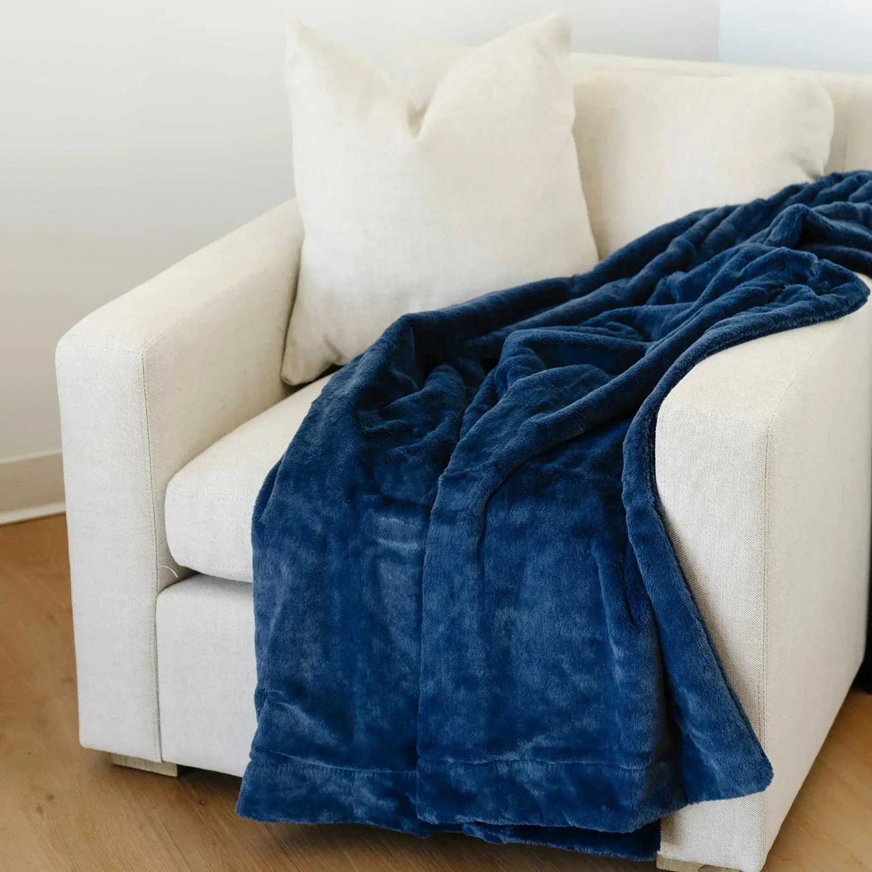 Blue blanket draped over a beige armchair in a room with wooden flooring.