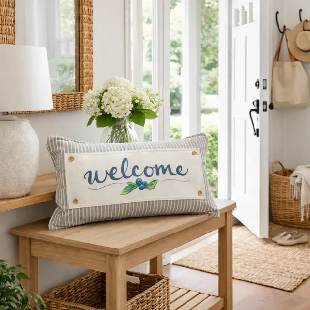 Decorative pillow with 'welcome' text on a wooden bench in a bright room.