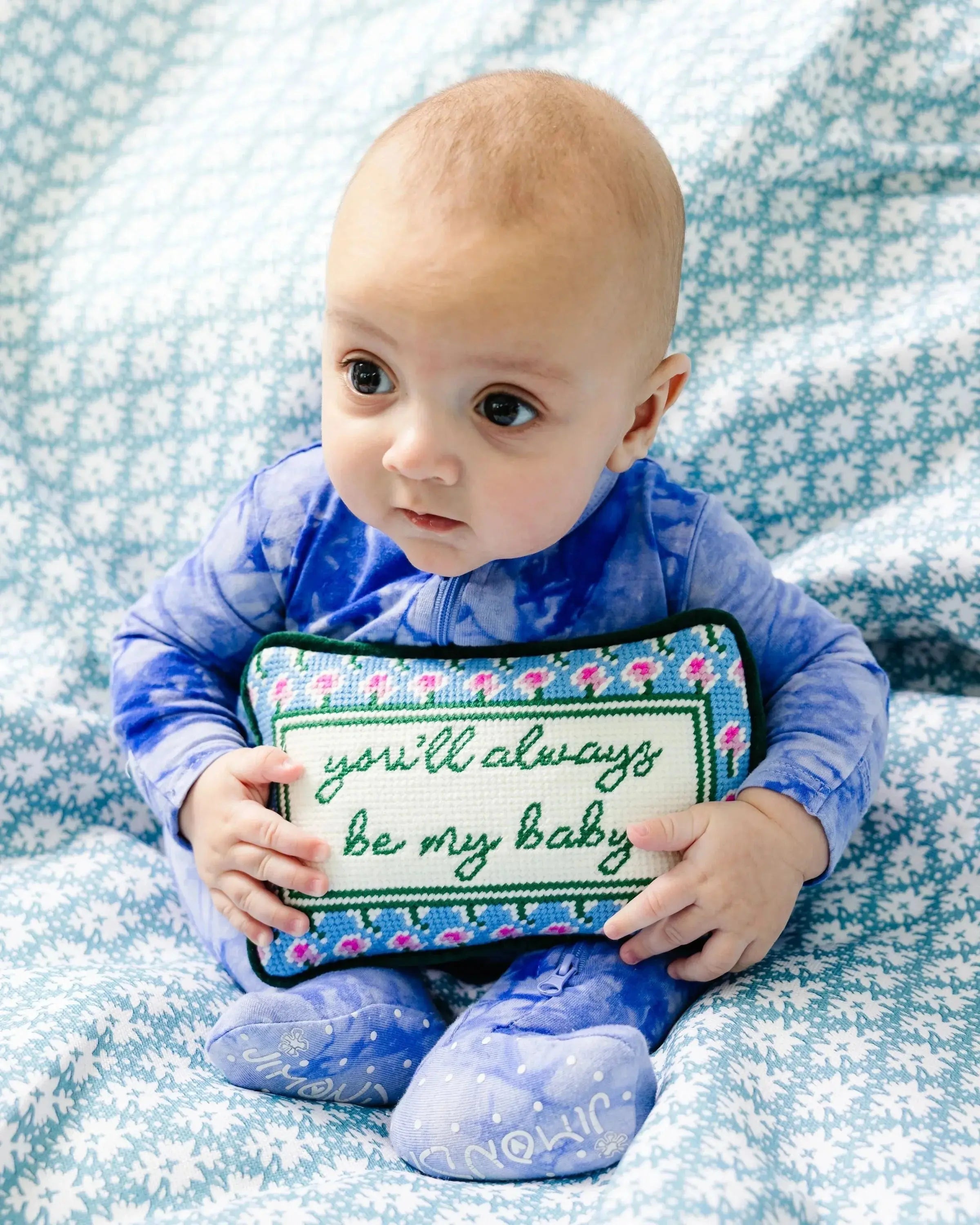 Baby holding 'you'll always be my baby' floral pillow on cozy patterned blanket