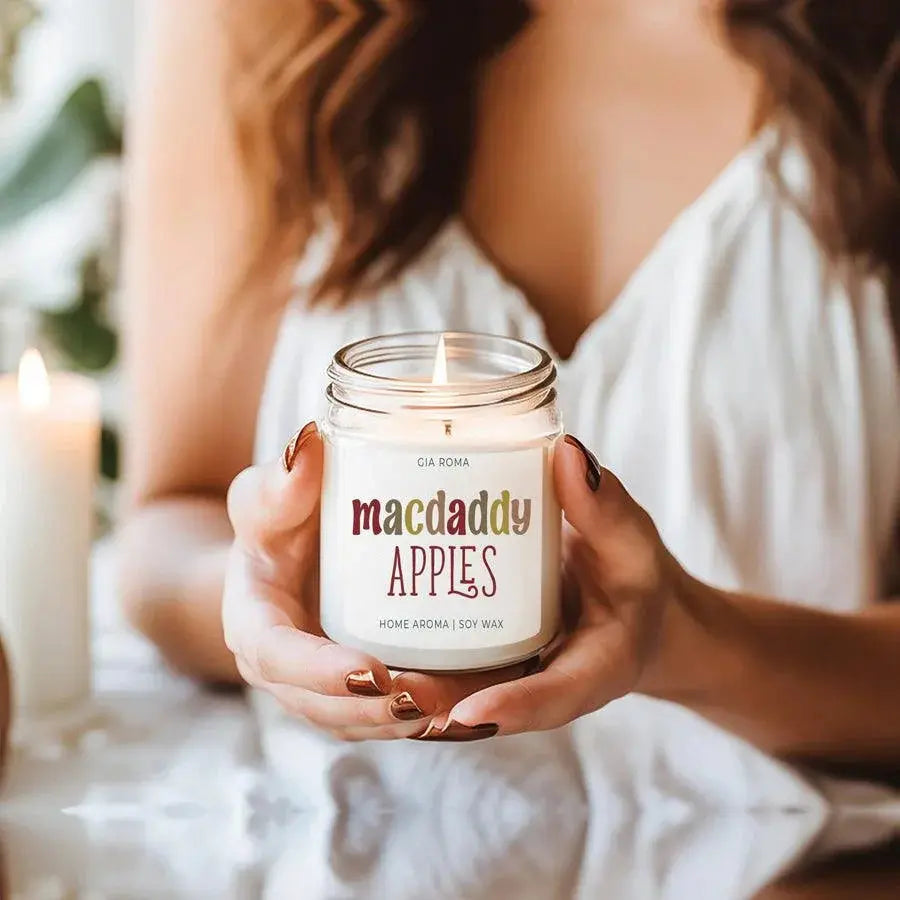 Person holding a 'comfy & cozy' candle jar with another candle in the background.