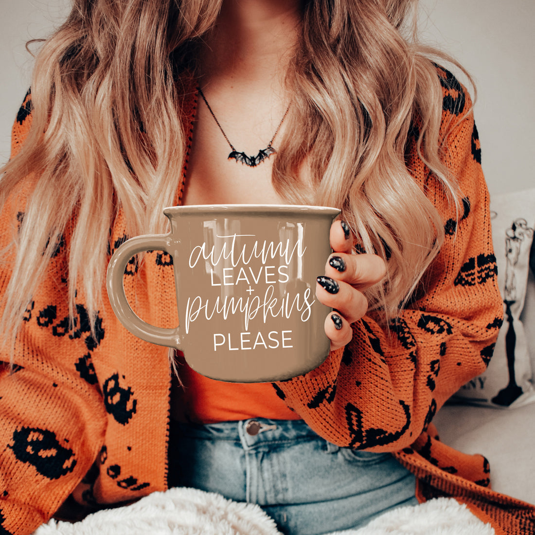 Person wearing an orange sweater with black patterns, holding a mug with text, sitting on a couch.