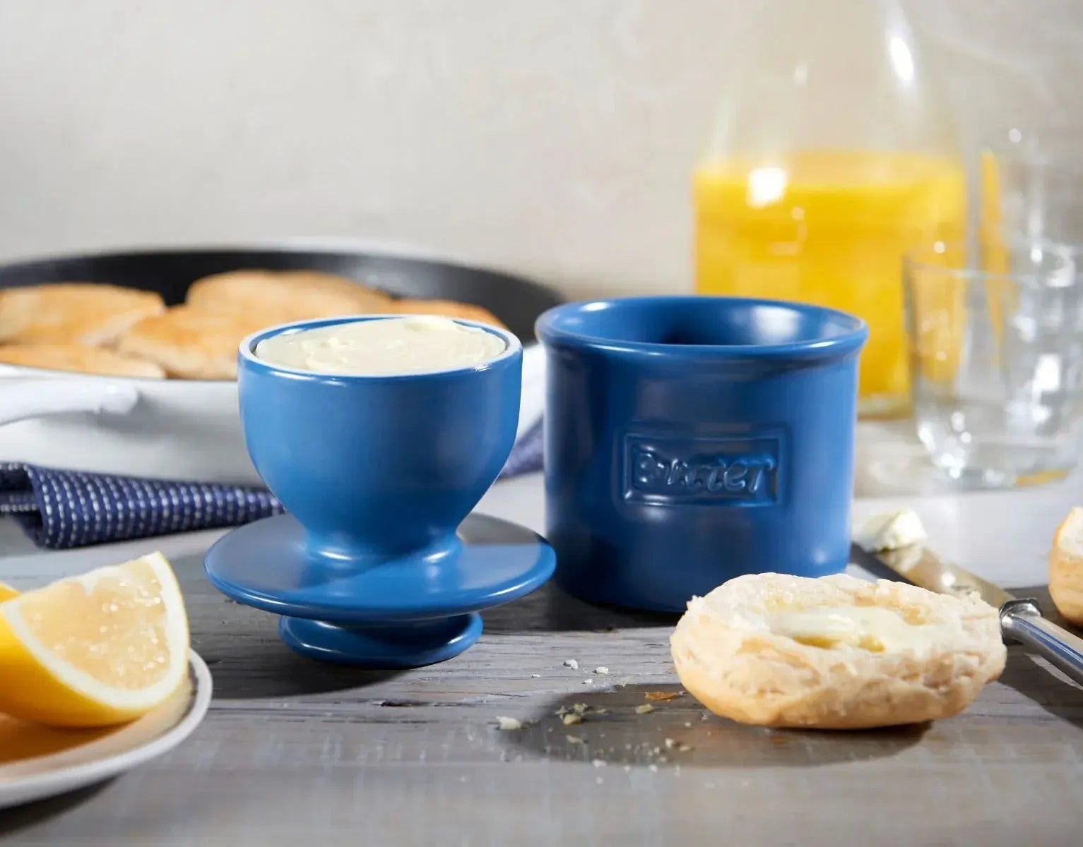 Blue ceramic butter dish with butter, biscuits, and lemon on rustic table for cozy farmhouse breakfast