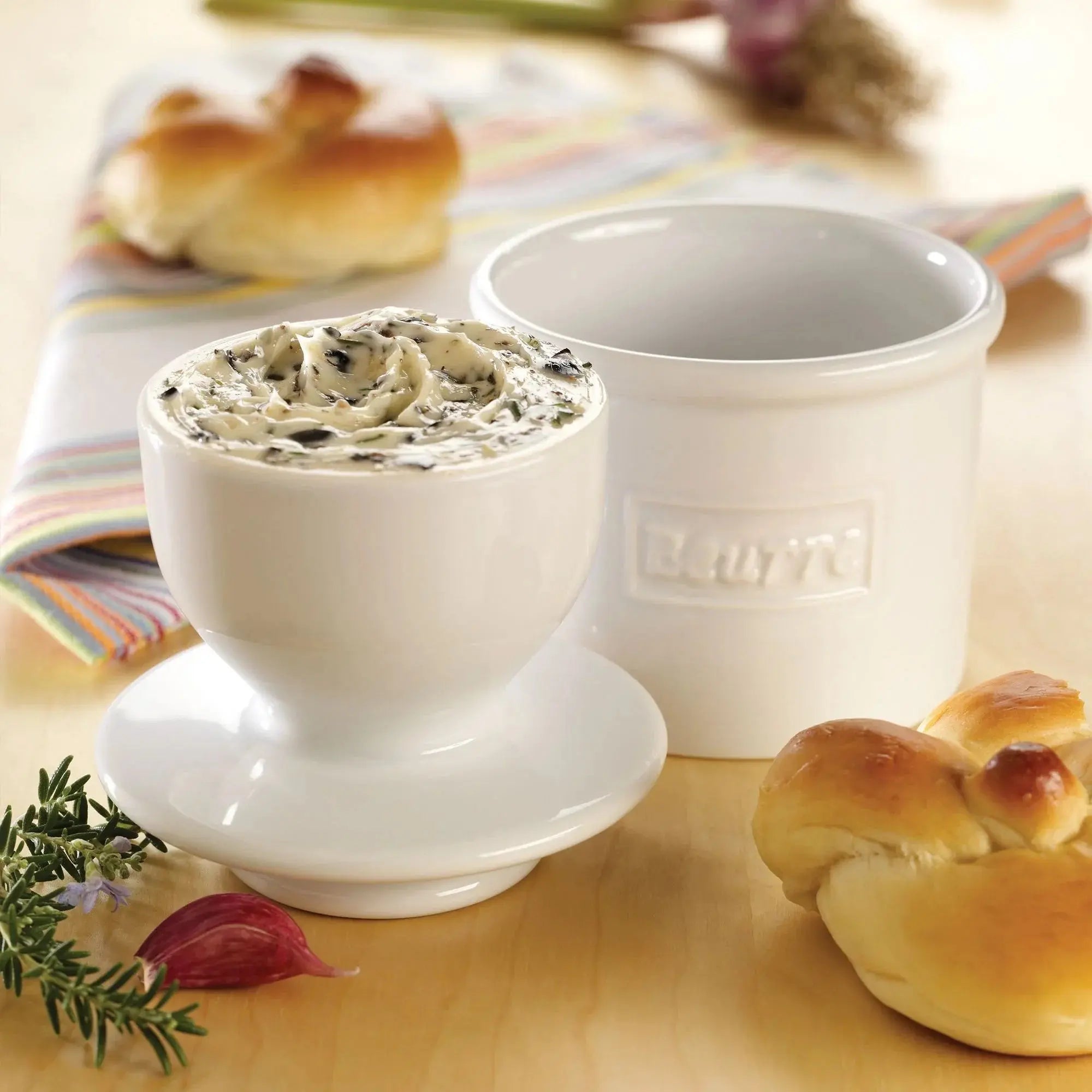 White ceramic butter dish with herb butter, fresh bread, and rosemary on wooden table