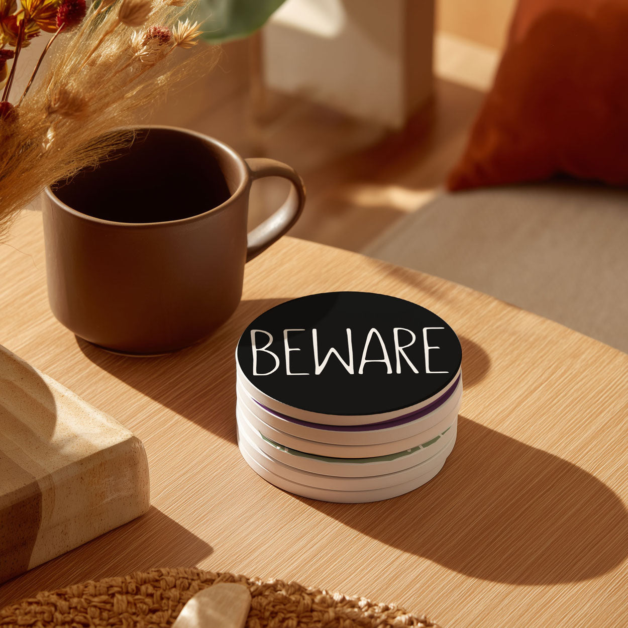 Stack of coasters with 'Beware' text on a table with a mug and decorative elements.