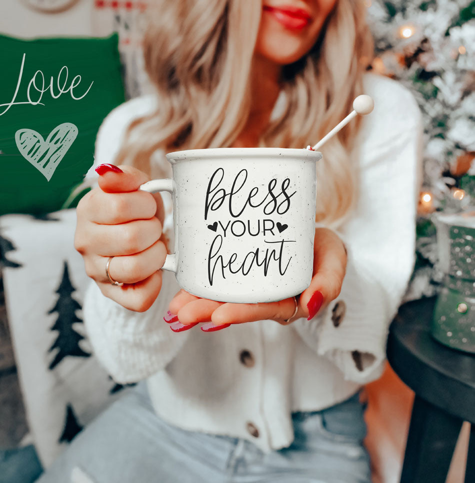 Person holding a mug with 'bless your heart' text in a cozy indoor setting.