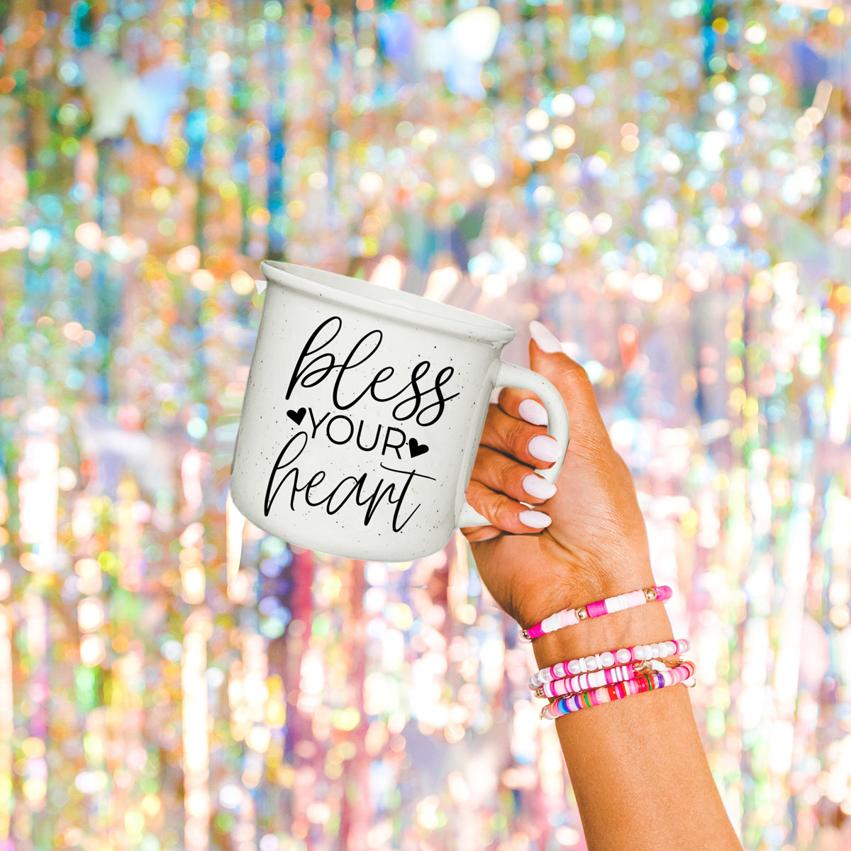 Hand holding a mug with 'bless your heart' text against a colorful, blurred background