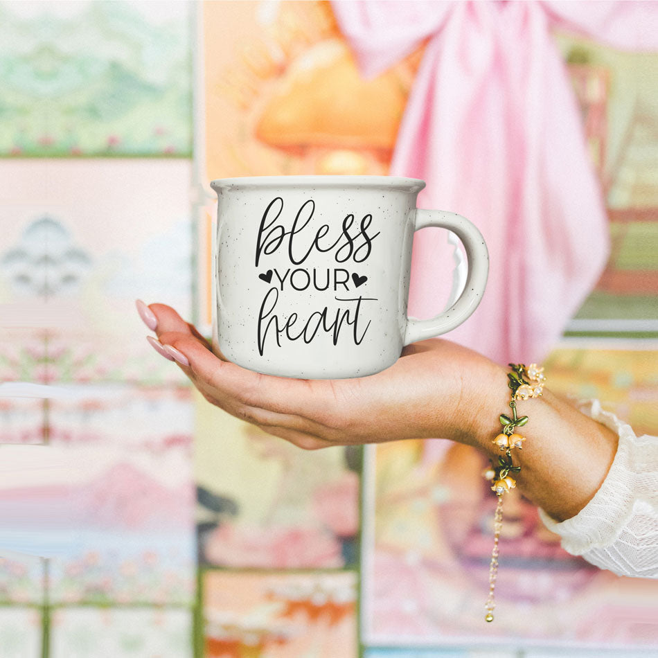 Hand holding a mug with 'bless your heart' text against a colorful, abstract background