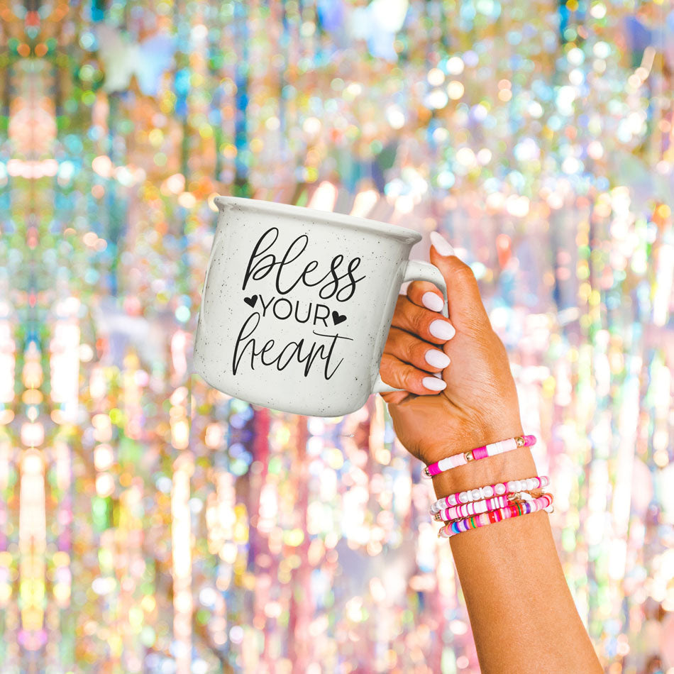 Hand holding a mug with 'bless your heart' text against a colorful, blurred background