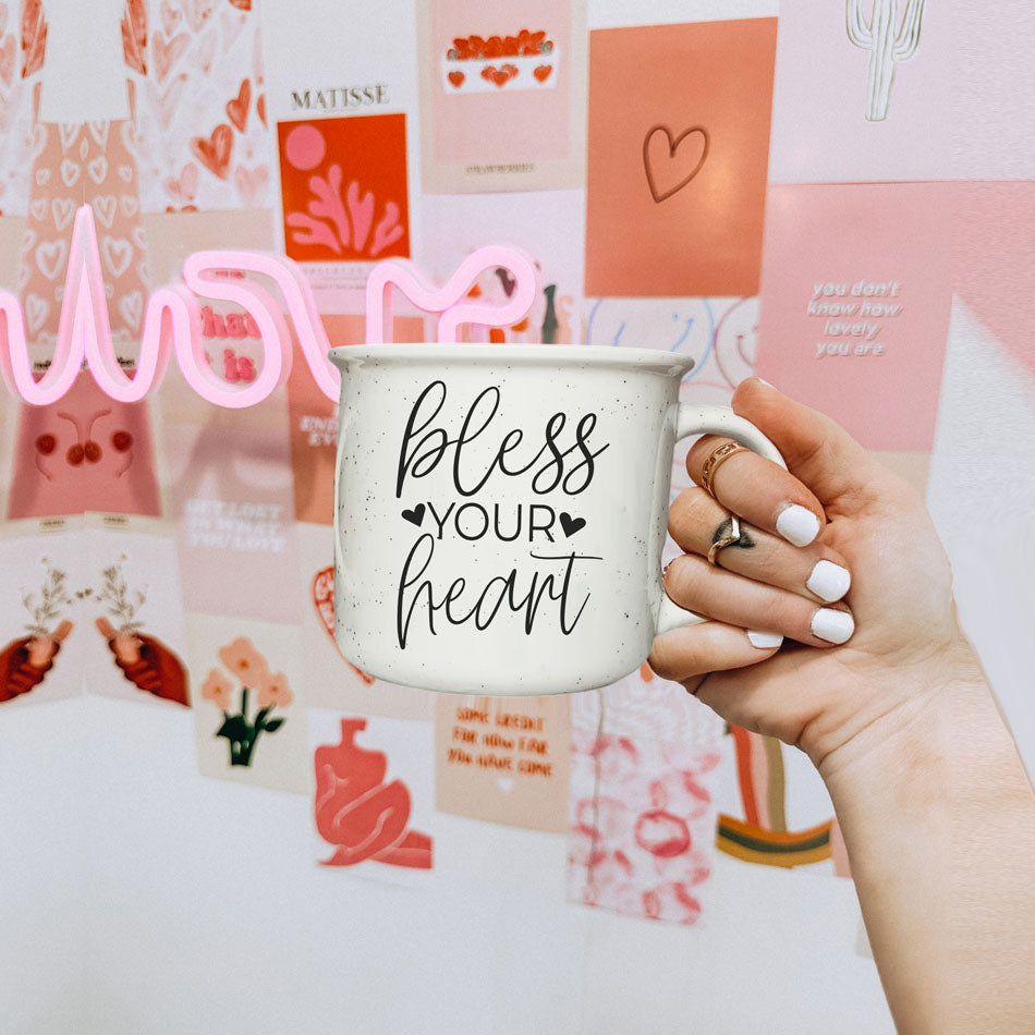Hand holding a mug with 'bless your heart' text against a colorful background