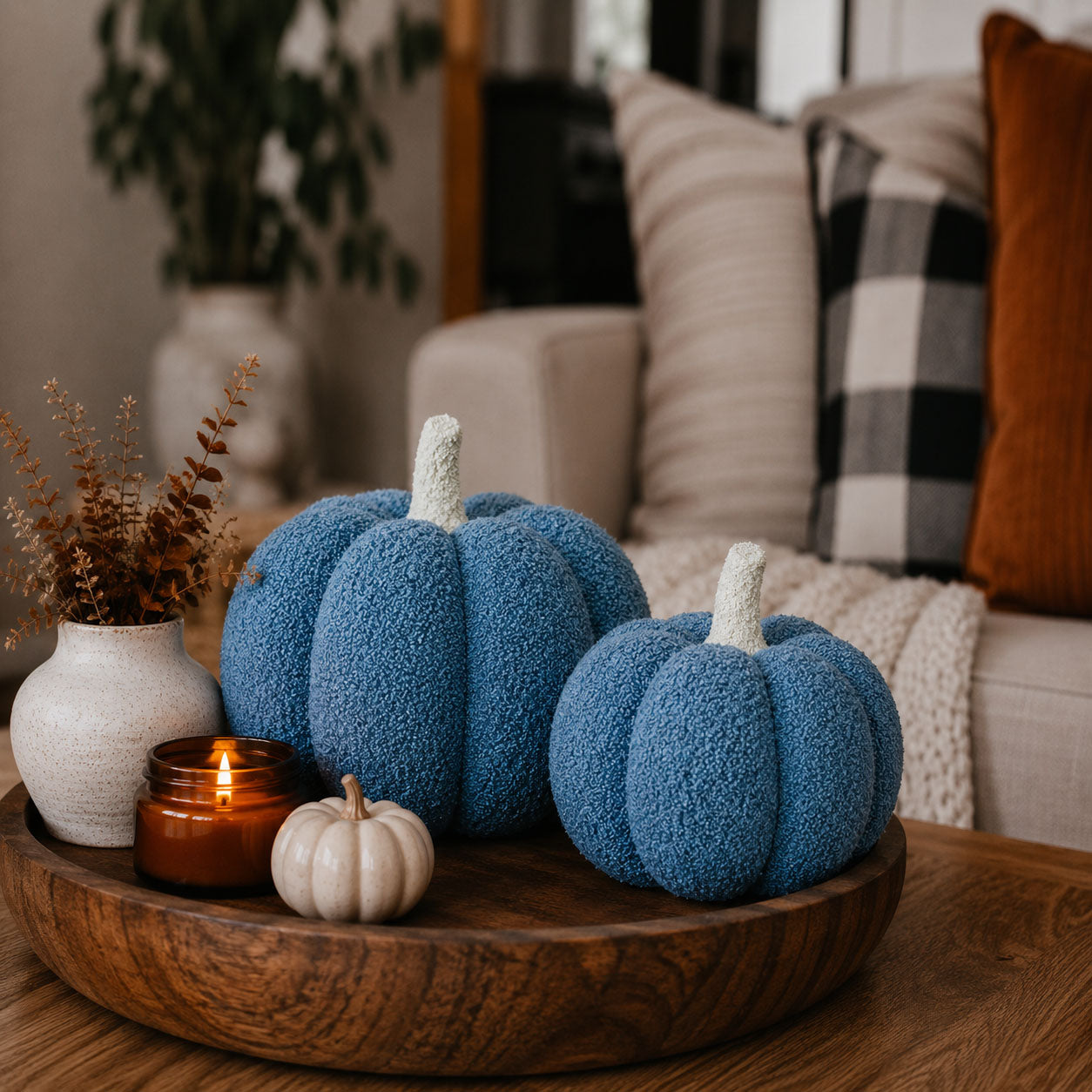 Decorative blue pumpkins on a wooden tray with a candle and small white pumpkin in a cozy living room setting.