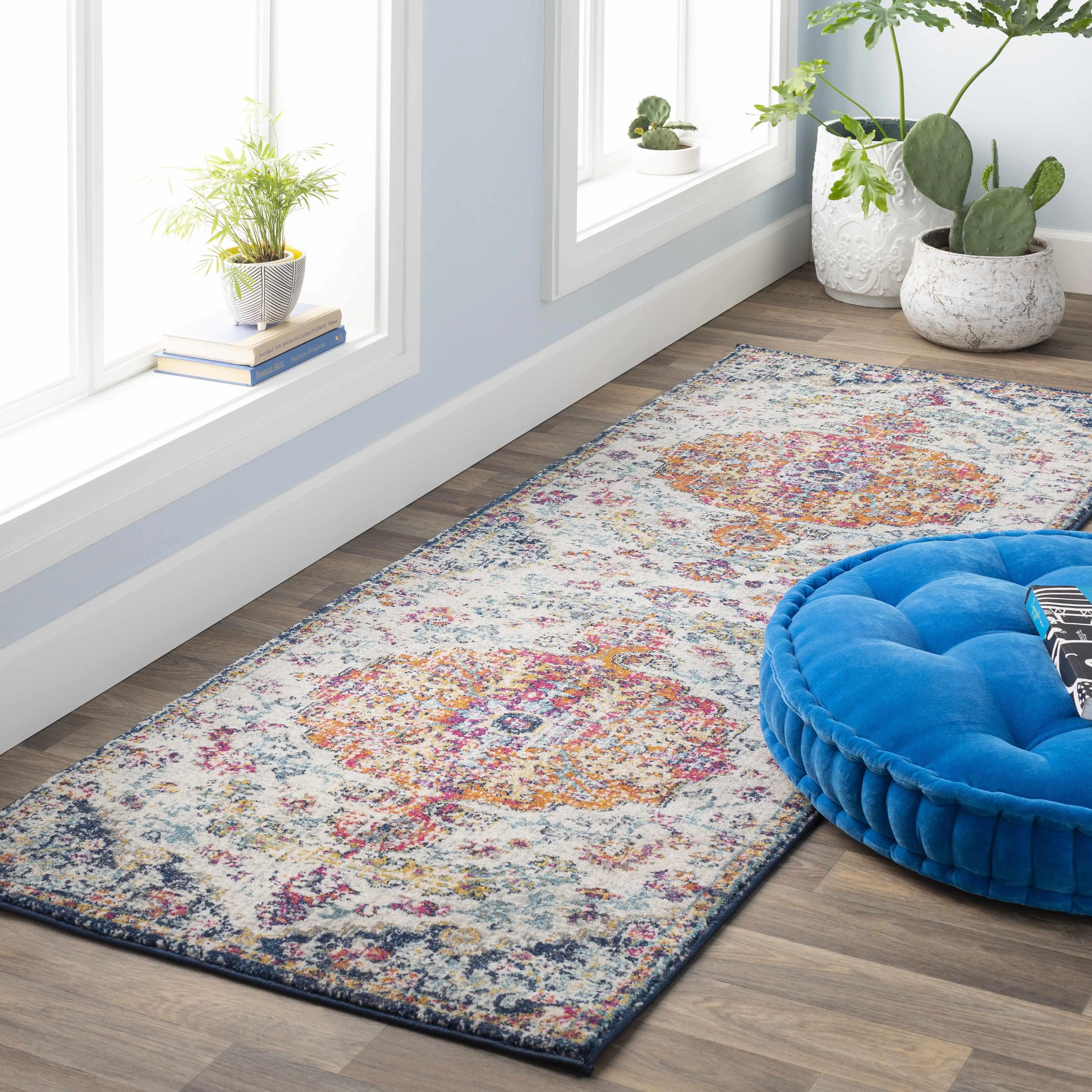 Colorful vintage-style area rug with floral patterns, paired with blue pouf and potted plants in cozy farmhouse decor.