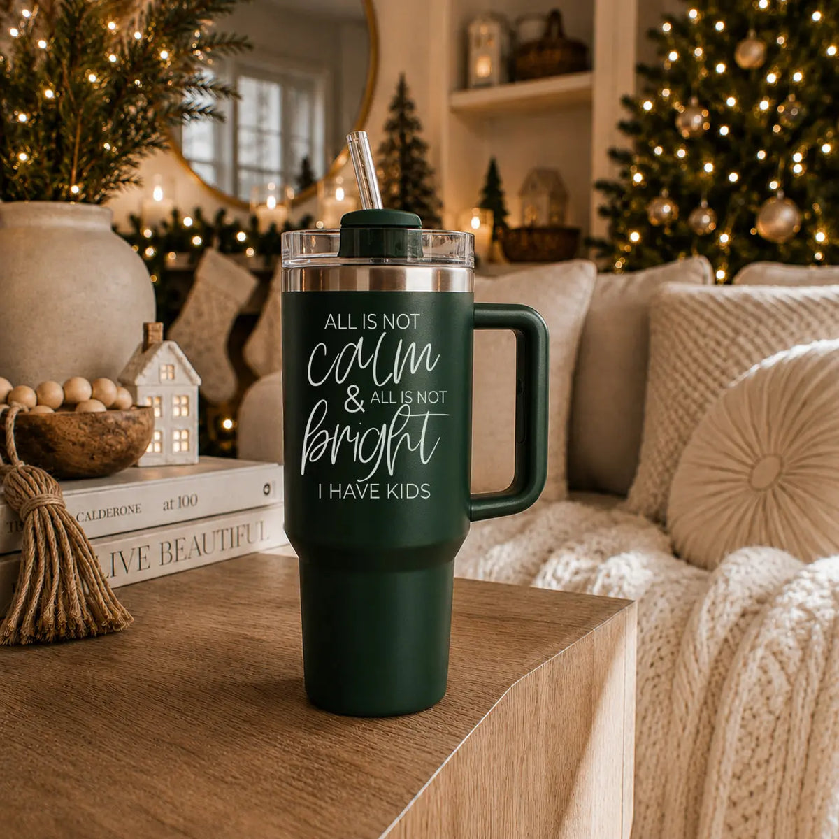 Green tumbler with text 'All is not calm & all is not bright. I have kids' on a wooden surface with Christmas decorations in the background.