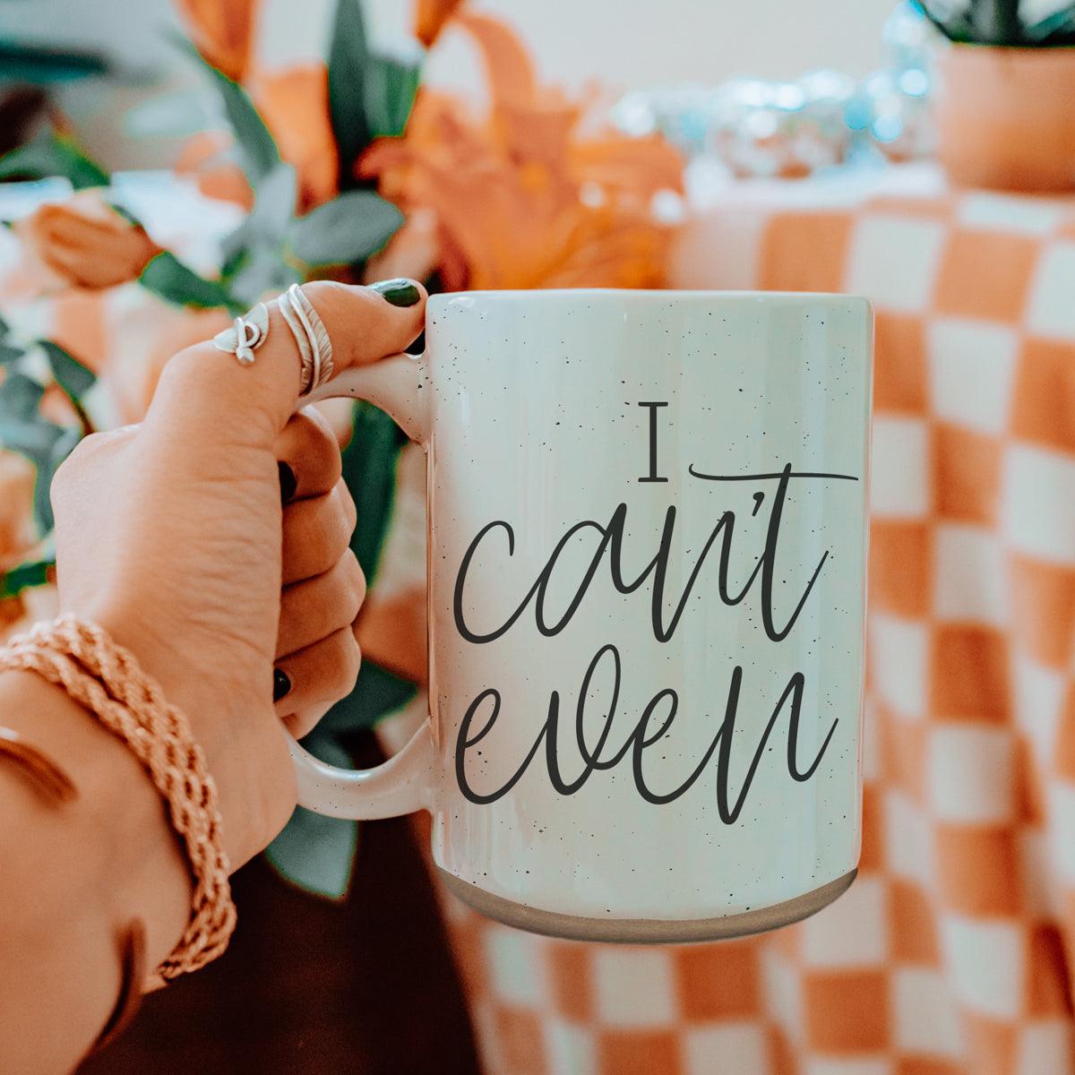 Hand holding a mug with 'I can't even' text against a blurred indoor background