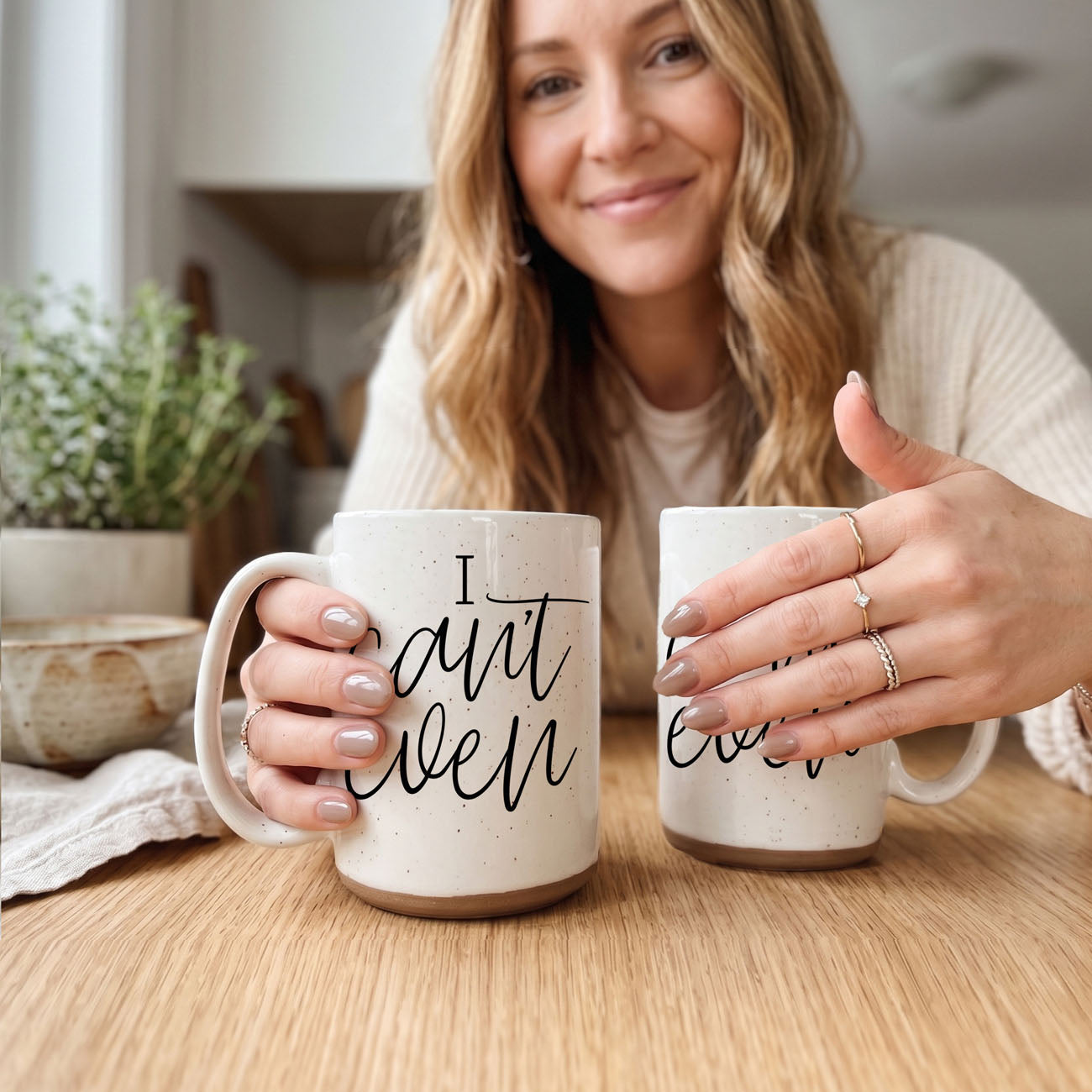 Woman holding two mugs with humorous text in a kitchen setting