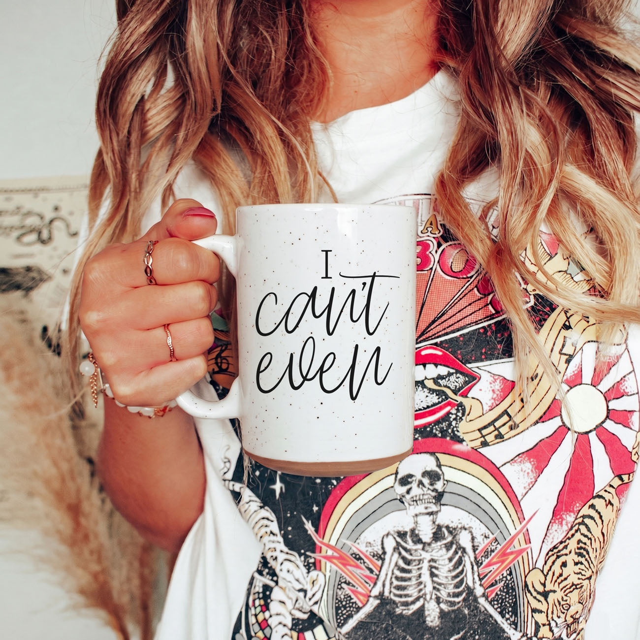 Person holding a mug with 'I can't even' text, wearing a colorful shirt with skeleton design.