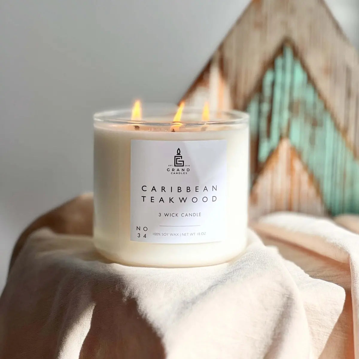 Caribbean Teakwood 3-wick soy candle burning on cozy fabric, farmhouse decor style