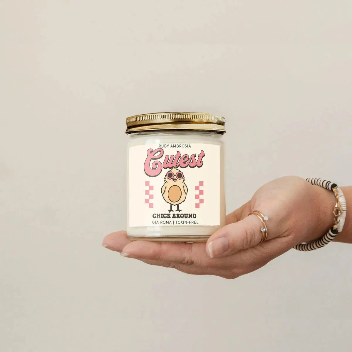 Hand holding a candle labeled 'Cutest Chick Around' with a neutral background