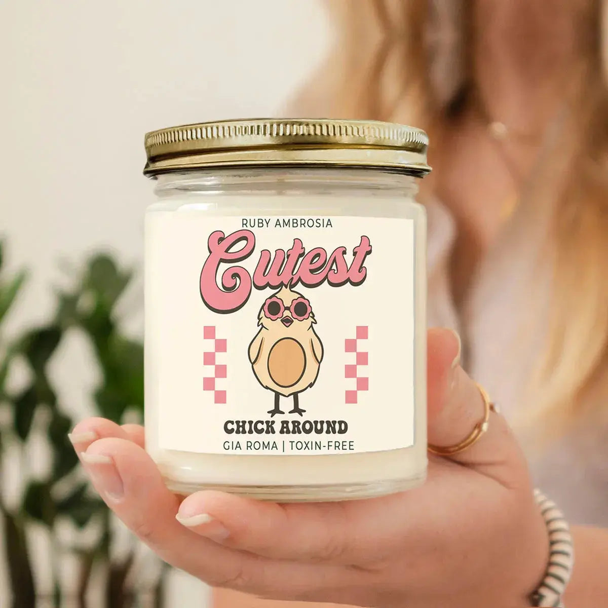 Hand holding a jar of Ruby Ambrosia 'Cutest Chick Around' candle with a blurred background