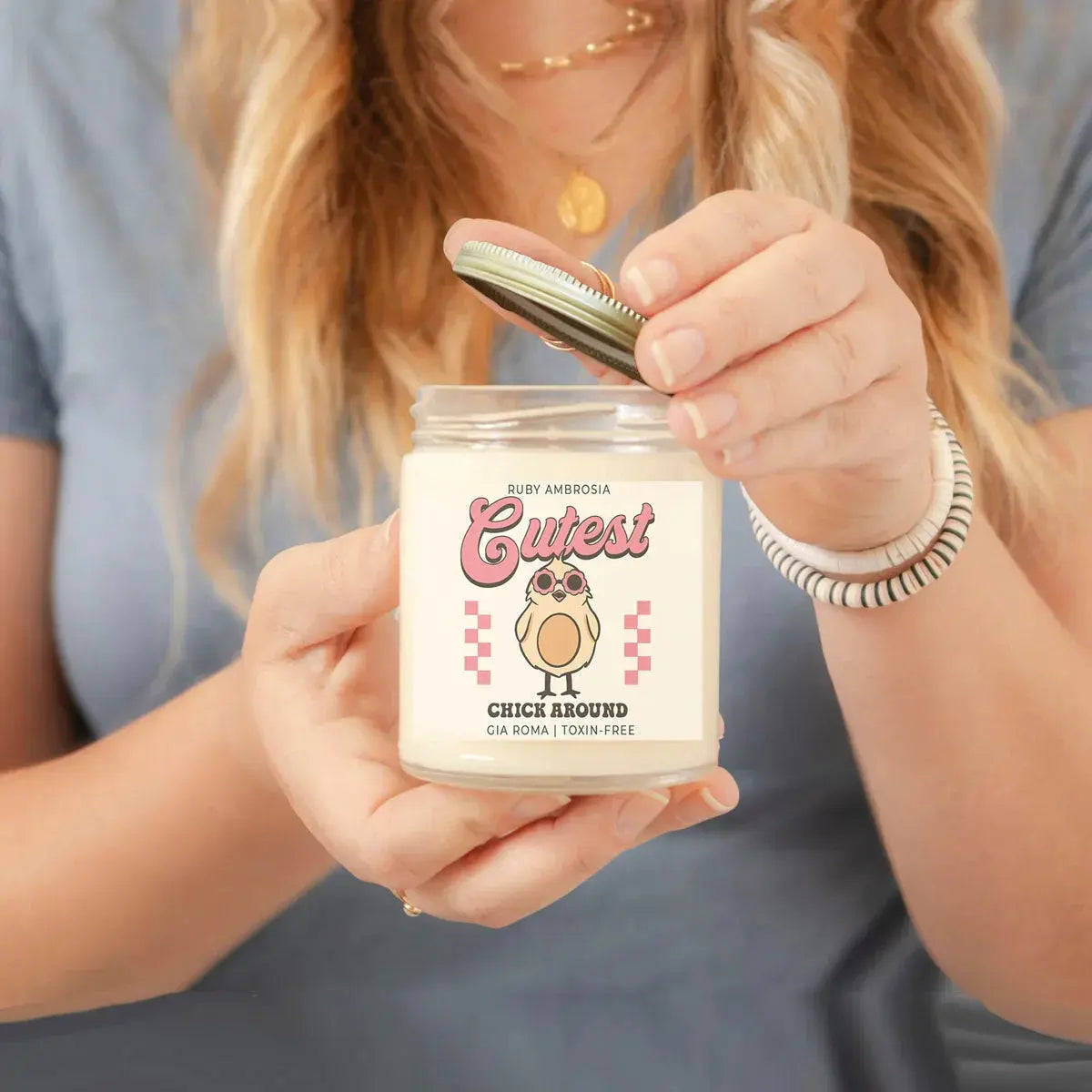 Person holding a candle jar labeled 'Cutest Chick Around' with a checkered design.