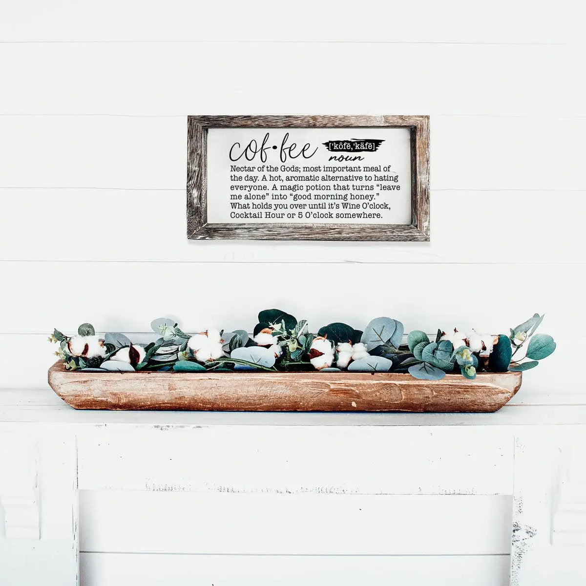 Decorative sign with text above a wooden tray with greenery on a white surface.