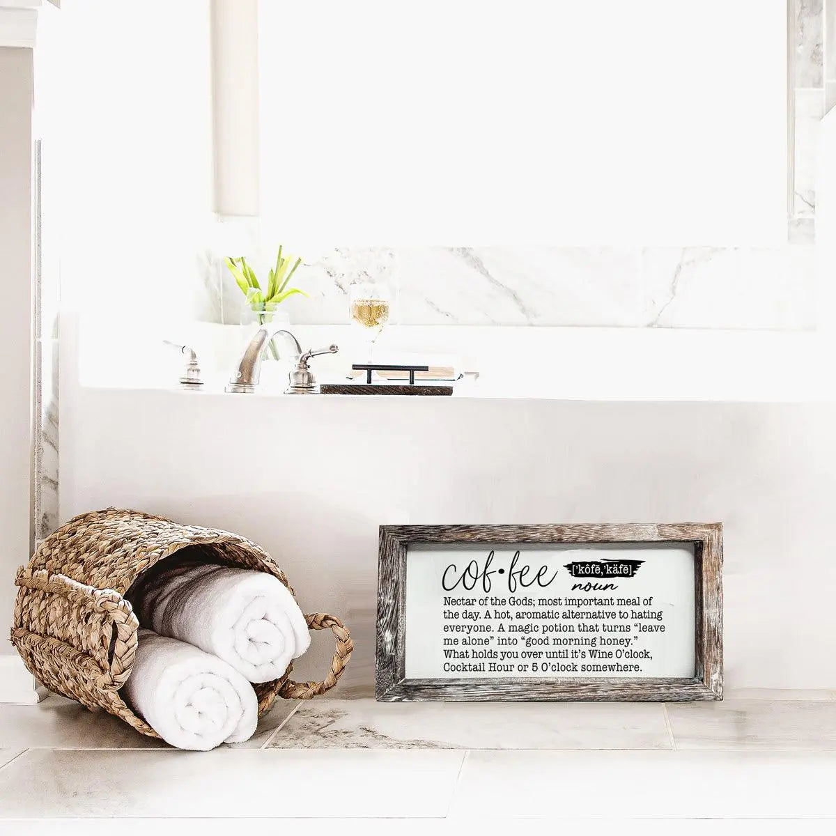 Wicker basket with rolled towels next to a framed sign on a bathroom counter.