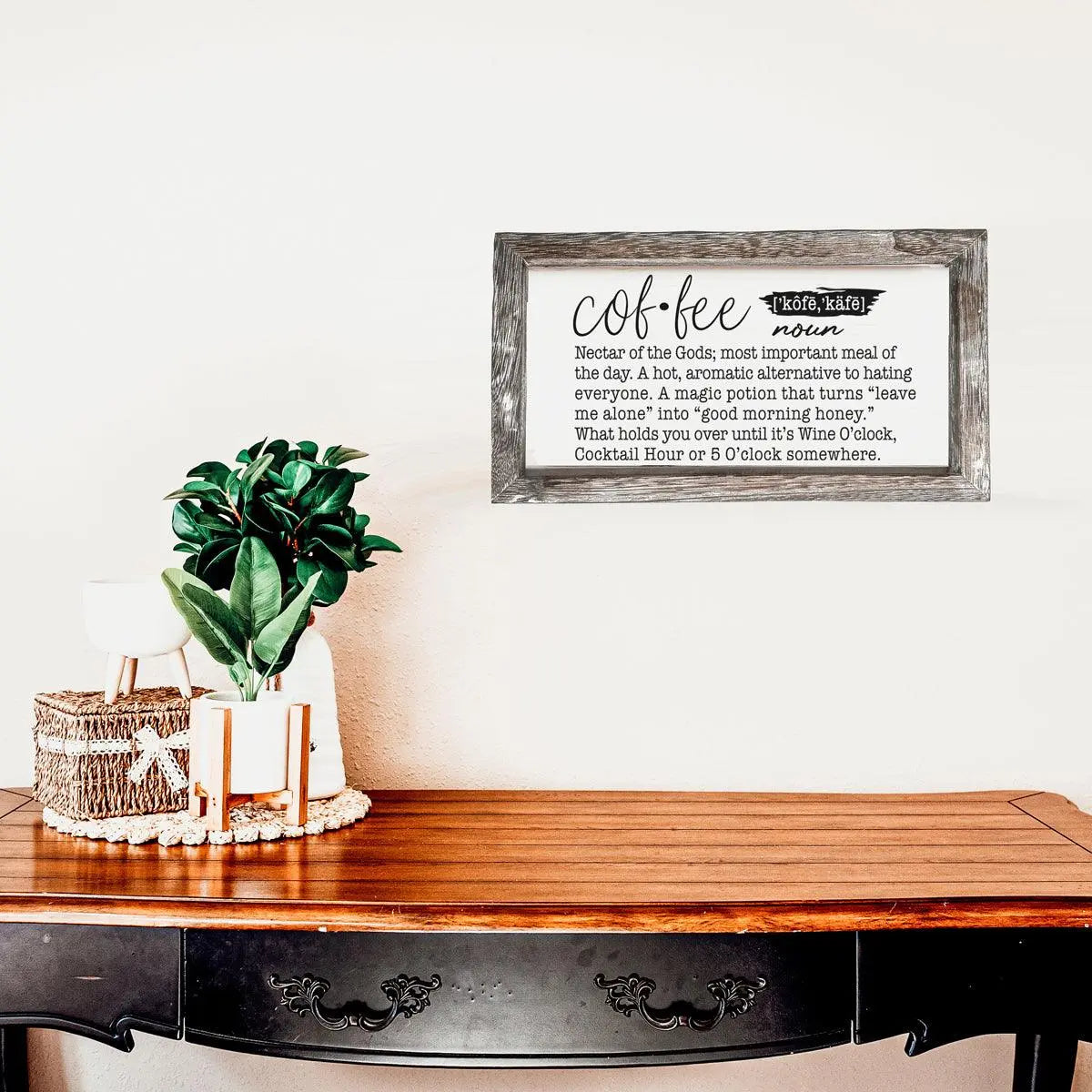 Decorative sign on a wall above a wooden table with a plant and basket.