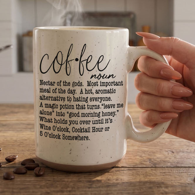 Mug with 'coffee' definition text held by a hand on a wooden surface.