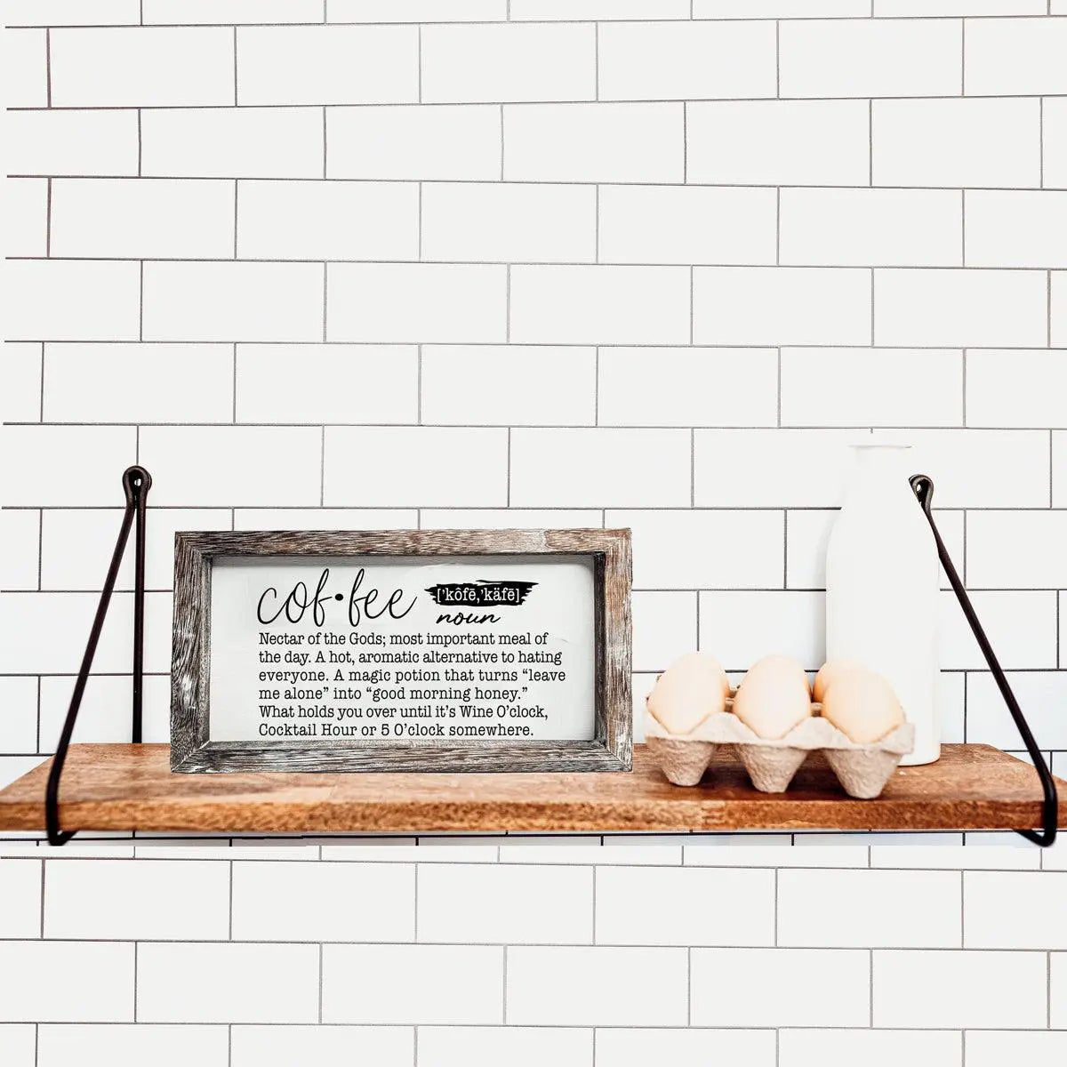 Wooden shelf with a framed sign and eggs against a white tiled wall