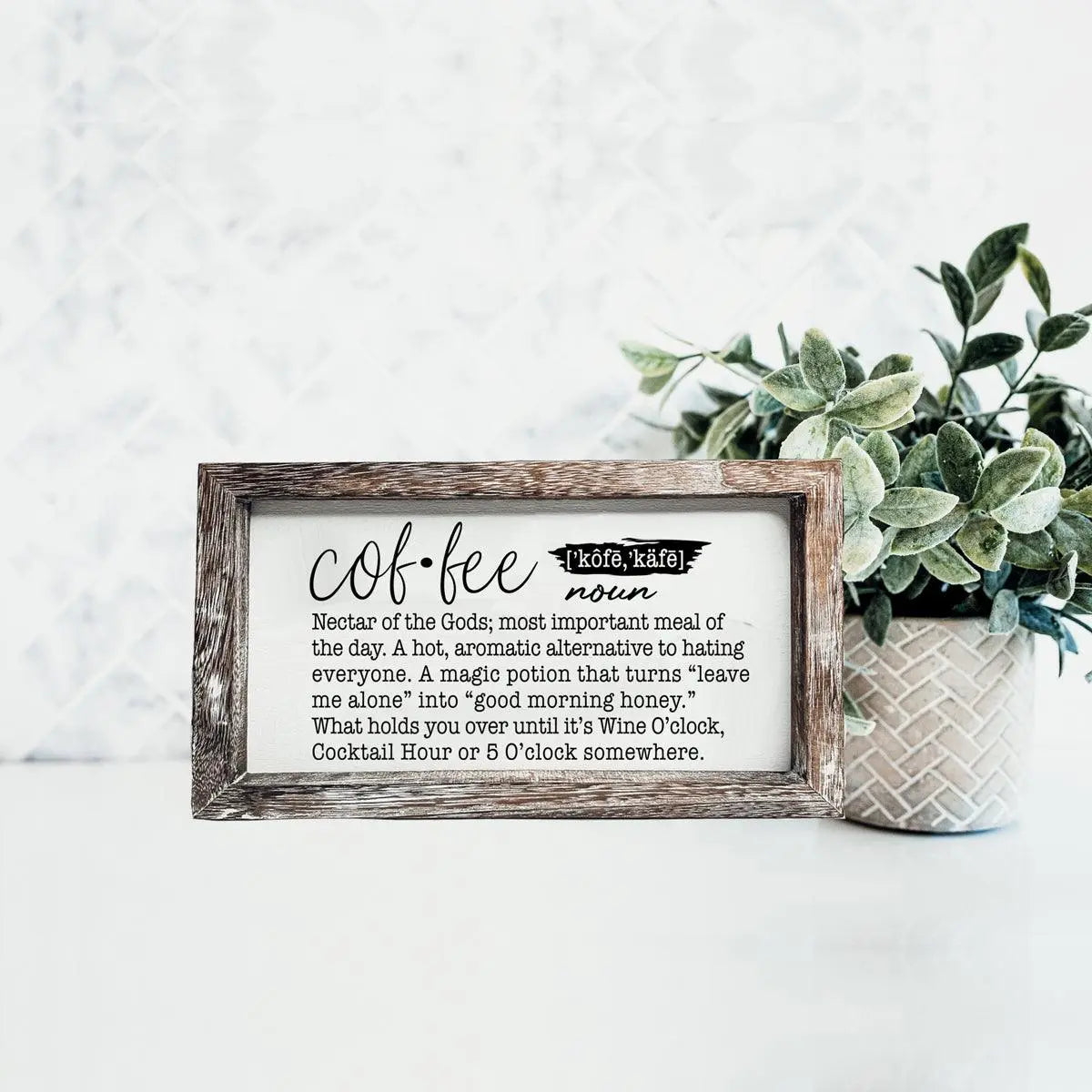 Decorative sign with coffee definition on a white surface with a plant in the background