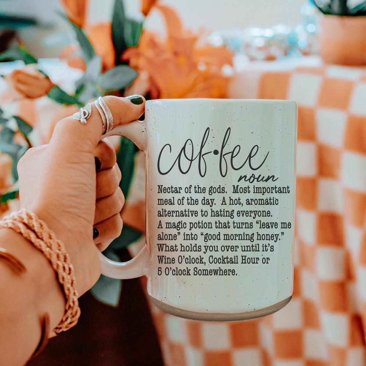 Hand holding a mug with 'Coffee' definition text against a blurred indoor background