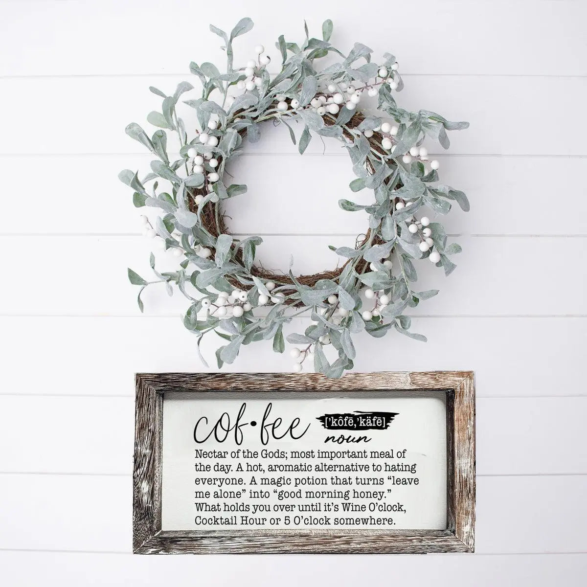 Wreath on a white wall with a framed sign below it.