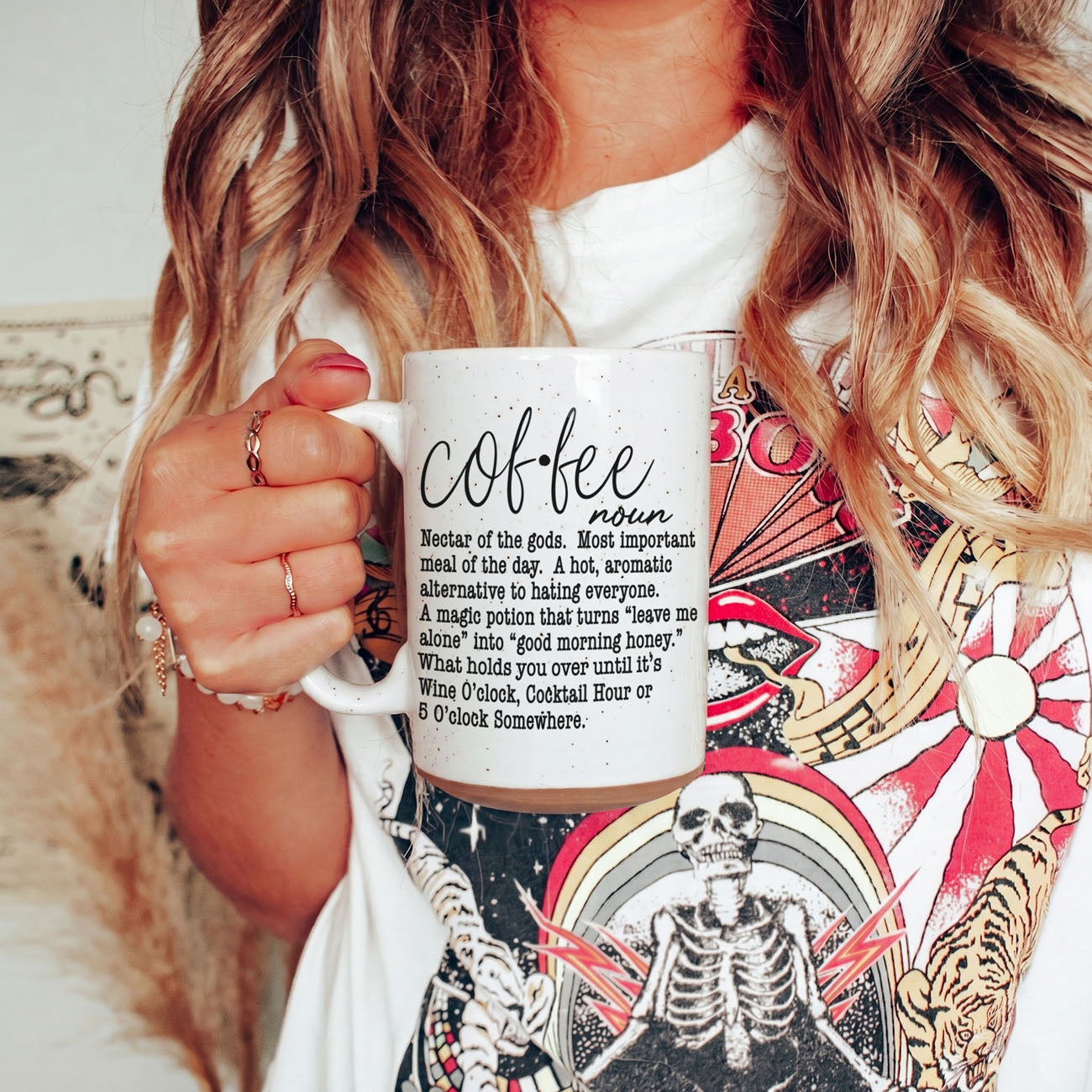 Person holding a mug with 'coffee' definition text, wearing a colorful shirt with skeleton design.