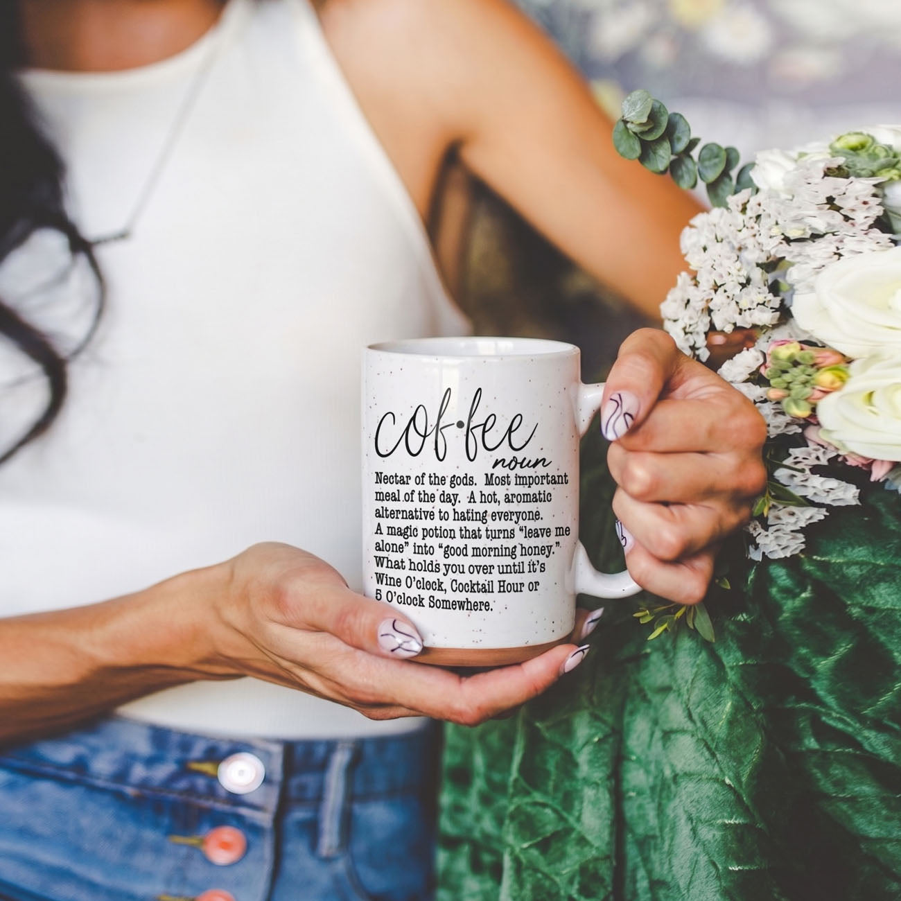 Person holding a mug with 'coffee' definition text, surrounded by flowers