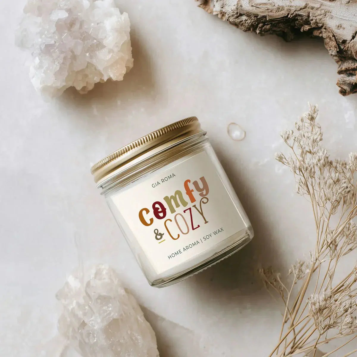 Candle jar labeled 'comfy & cozy' on a marble surface with crystals and dried plants.