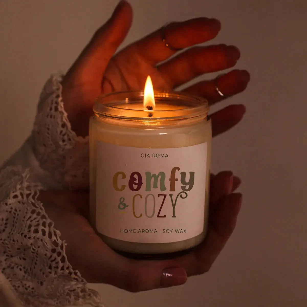 Candle labeled 'comfy & cozy' held by a hand with a warm glow.
