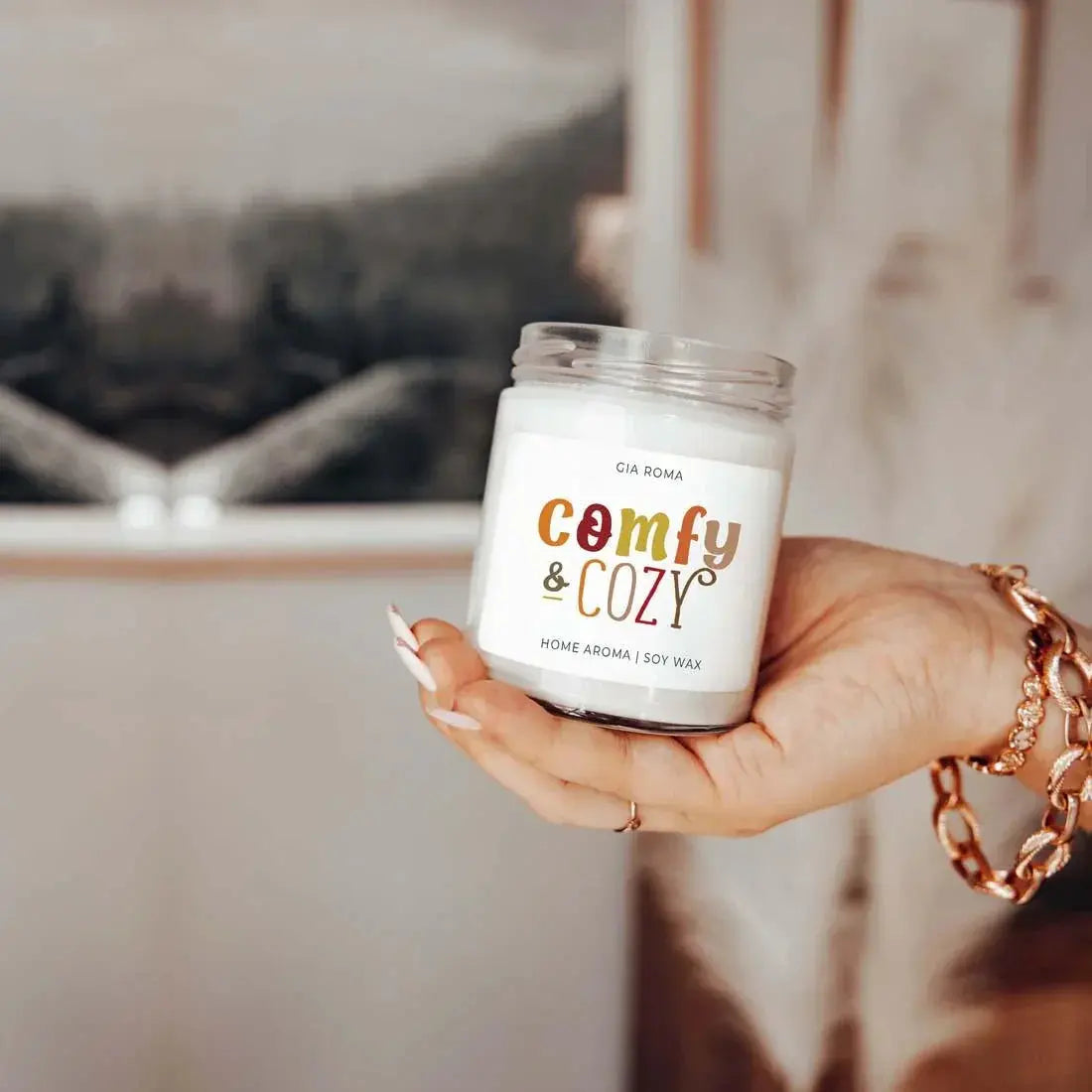 Hand holding a 'comfy & cozy' candle with a blurred background
