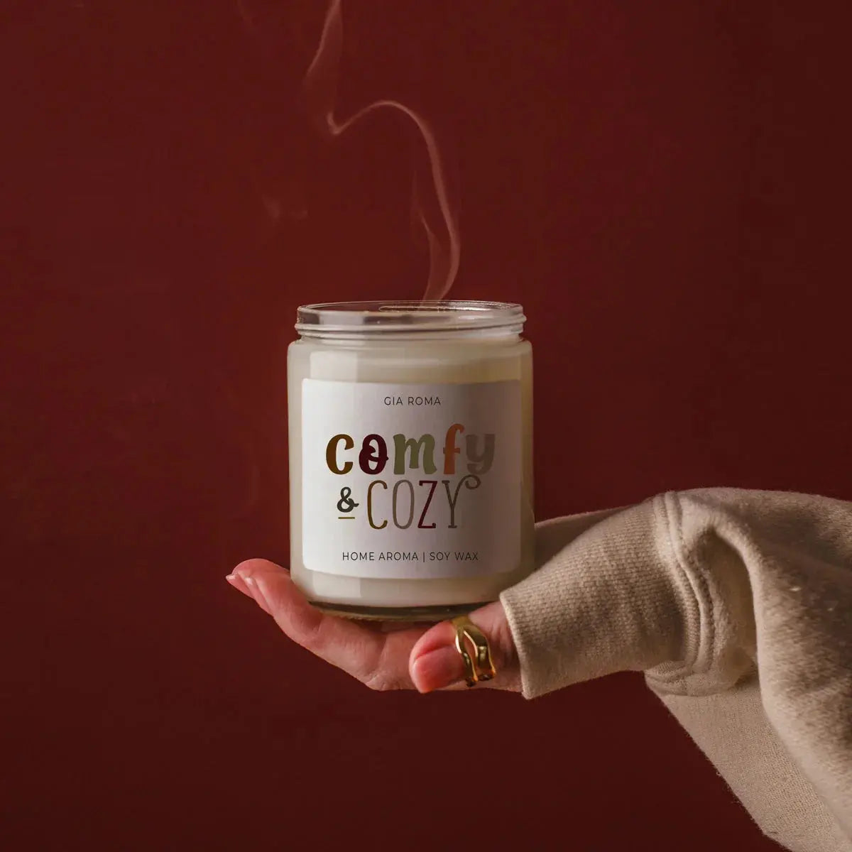 Hand holding a 'comfy & cozy' candle against a dark background